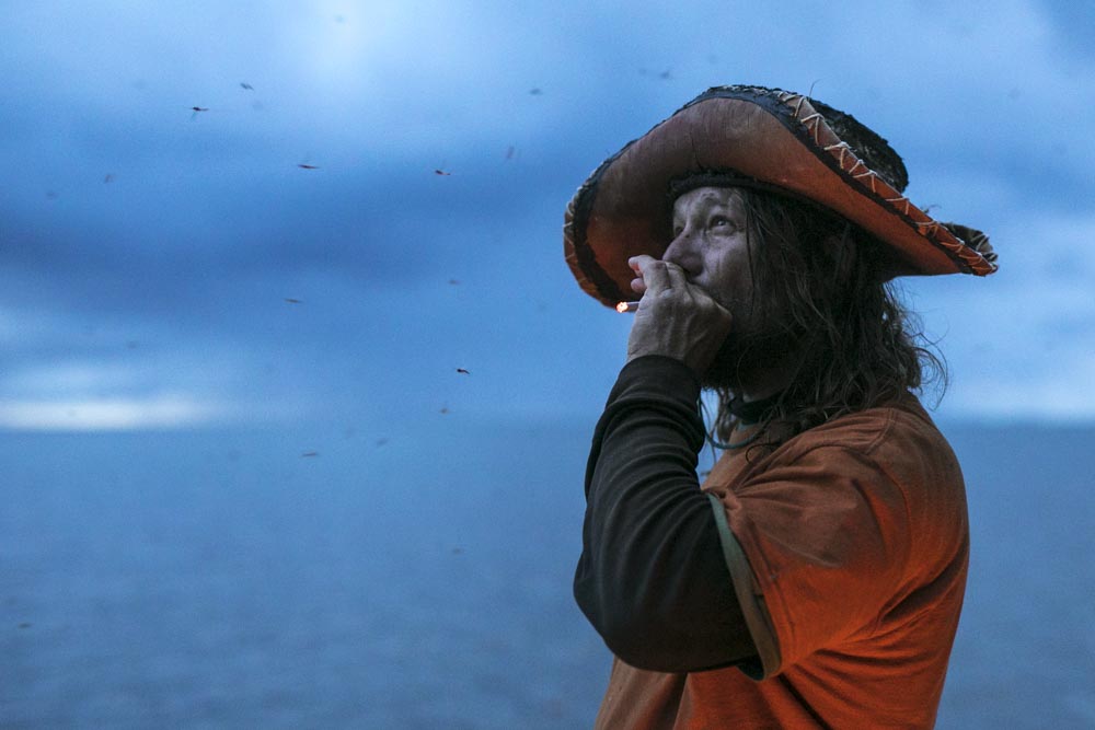 June 29, 2017.
Low on food, plagued by winds, and silenced by the roar of a million bugs, Mike Ranta smokes a cigarette and considers the wind problems he'd been experiencing on Cedar Lake, Manitoba.
In 2014, Mike Ranta became the first person in history to canoe from the Pacific to Atlantic ocean in a single season, alone, by canoe. Clad in a Métis sash, slaving under his birch bark hat and alongside his canine, Spitzii, the jovial masochist endured 214 days and roughly 8,000 kilometres to achieve the unprecedented goal. In 2016, Ranta found a faster route and bested his own record by fourteen days. Born and raised in Atikokan, Ontario, the forty-five year old was inspired by the tales of voyageurs who fuelled the North American fur trade for nearly 300 years with their unbridled resilience. In 2017, the self proclaimed ‘modern voyageur’, departed Bella Coola, British Columbia, to attempt one final coast-to-coast trip. With months lost to harrowing weather and pitiless wind, after 187 days of obsessed desire, Ranta would quit on Lake Superior, Ontario, at the base of a gale force storm. For the man who could wander the halls of his accolades, on a trip marred by hardship, only one proof remains of Mike Ranta; the journey is the adventure.