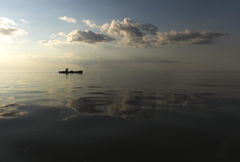 Meeting a few big fans on the water and adding under calm skies and reflective water, Mike Rata paddles all day and becomes wind bound by night fall on Lake Winnipeg, Manitoba. 20170804. Photo/David Jackson