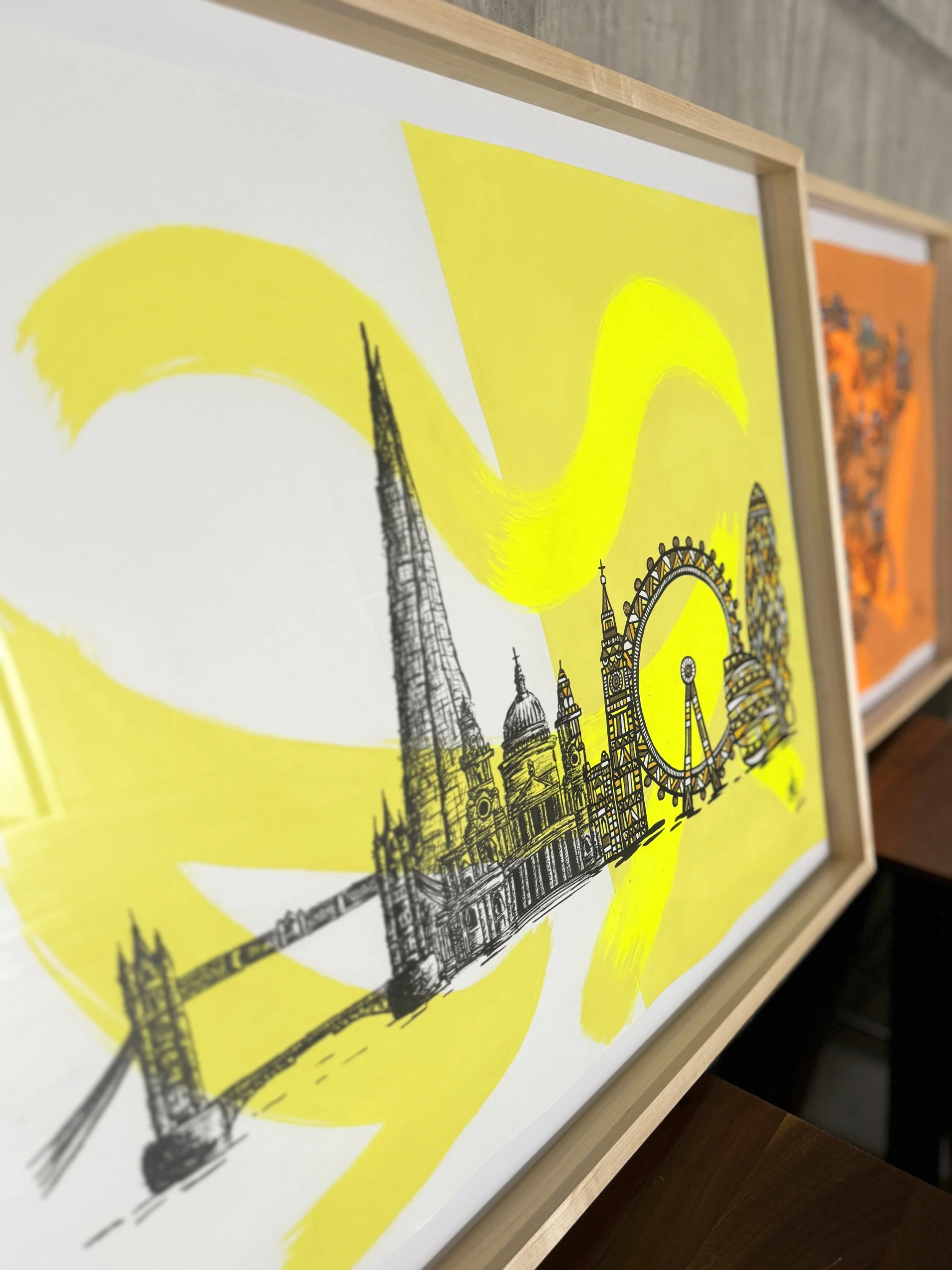 Framed artwork of London landmarks including Big Ben, the London Eye, and Tower Bridge, with yellow paintbrush strokes in the background.