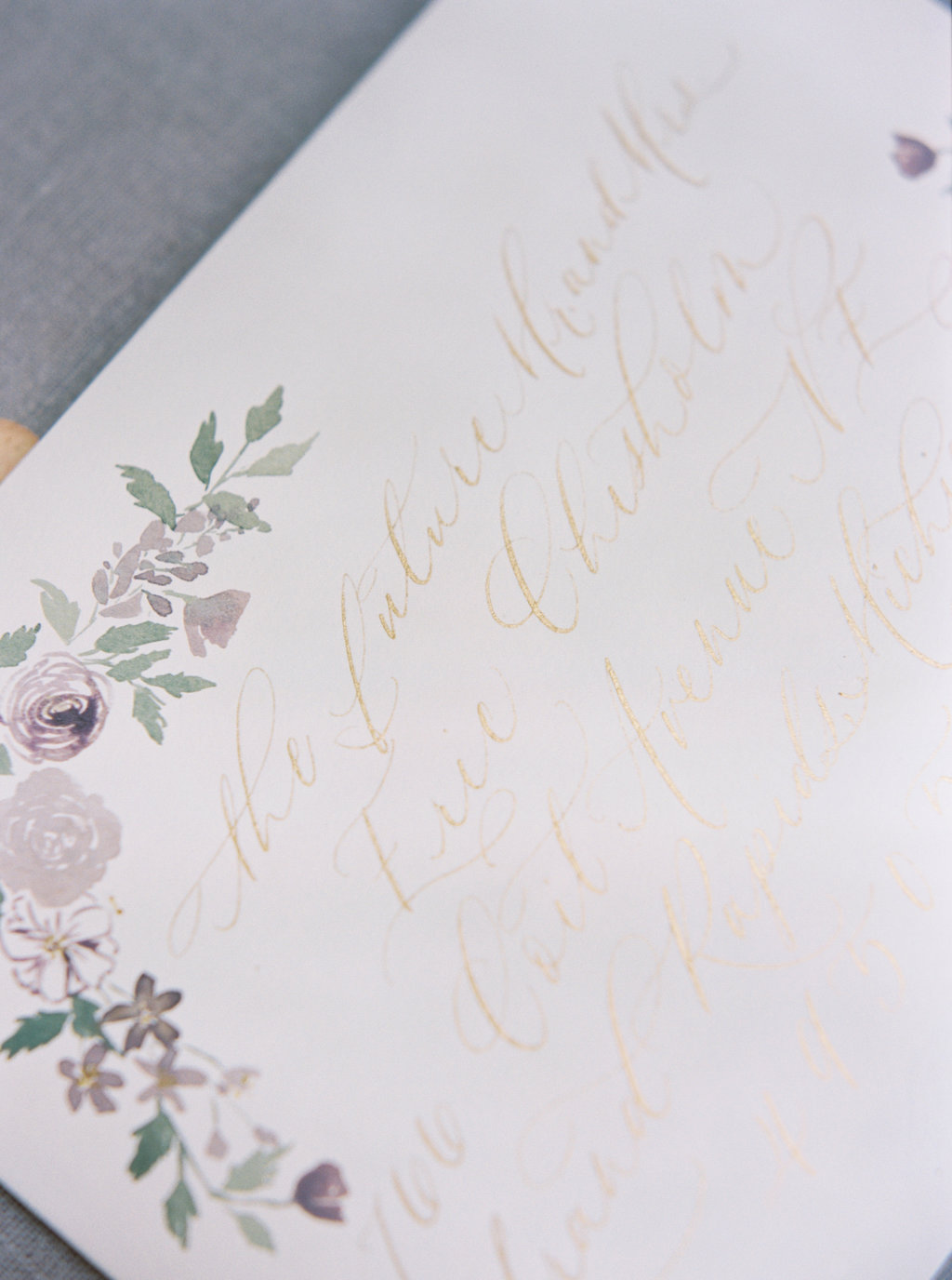 Gold calligraphy and watercolor flowers on wedding envelopes.