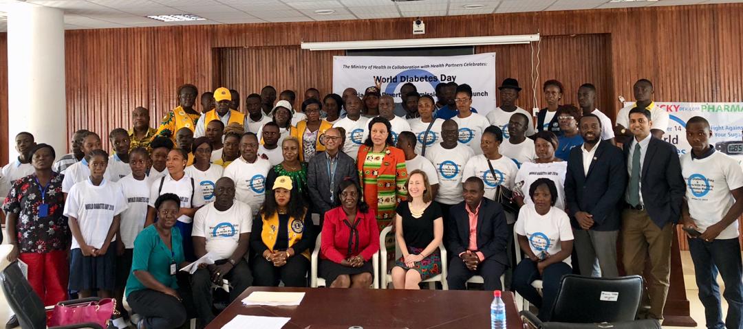 MRS. JOYCE SHERMAN (CENTER OF FIRST ROW STANDING), ASSISTANT MINISTER OF PREVENTIVE SERVICES FOR LIBERIA’S MINISTRY OF HEALTH AND SOCIAL WELFARE, LAUNCHED THE LIBERIA NCDI POVERTY COMMISSION’S REPORT AT A WORLD DIABETES DAY EVENT AT MOHSW HEADQUARTERS IN MONROVIA. COMMISSION CO-CHAIR DR. FRED AMEGASHIE (3RD FROM RIGHT IN FIRST STANDING ROW) PRESENTED KEY FINDINGS FROM THE REPORT.