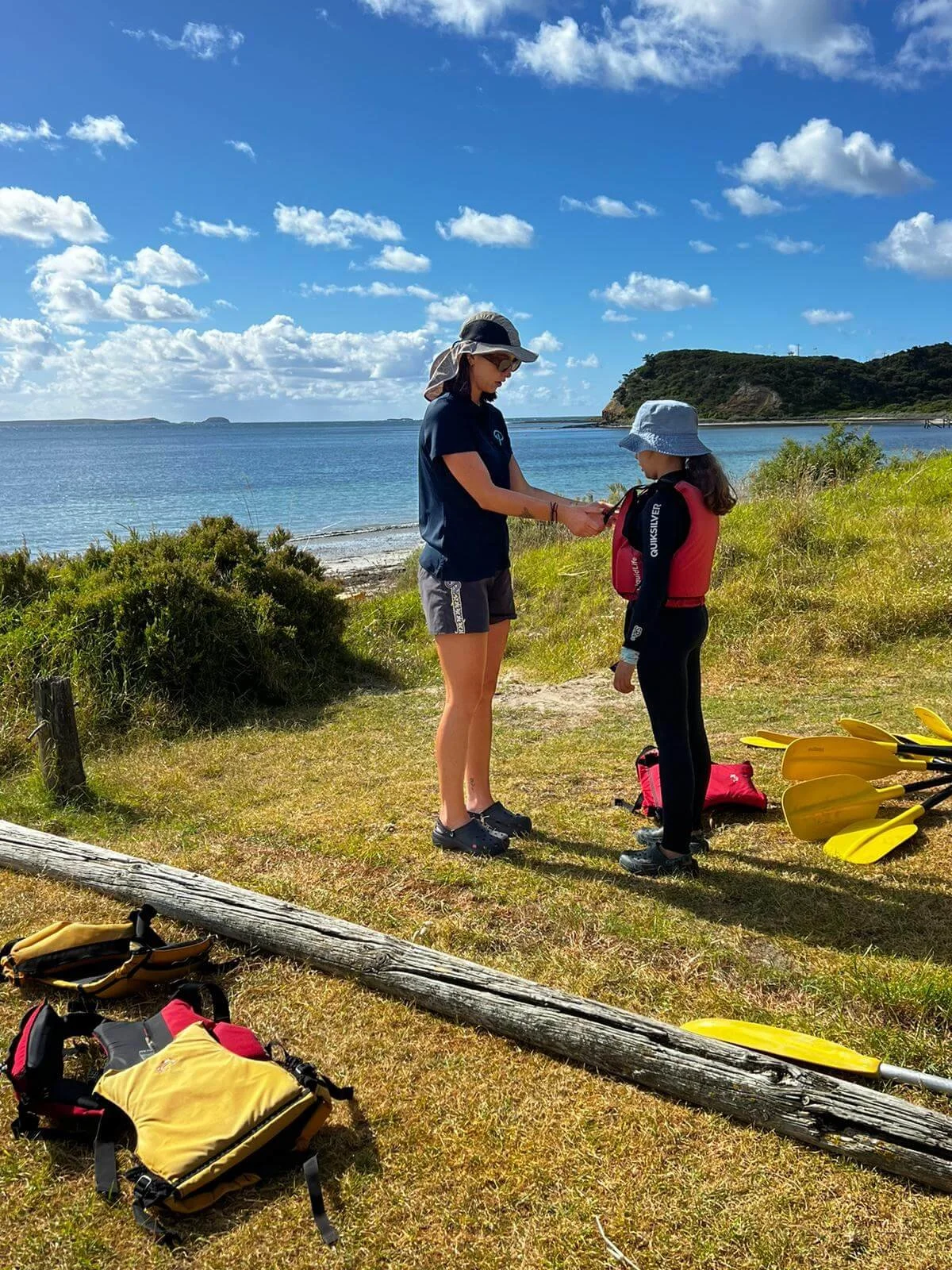 Summer camp instructor helping a student adjust her life jacket before a canoeing activity