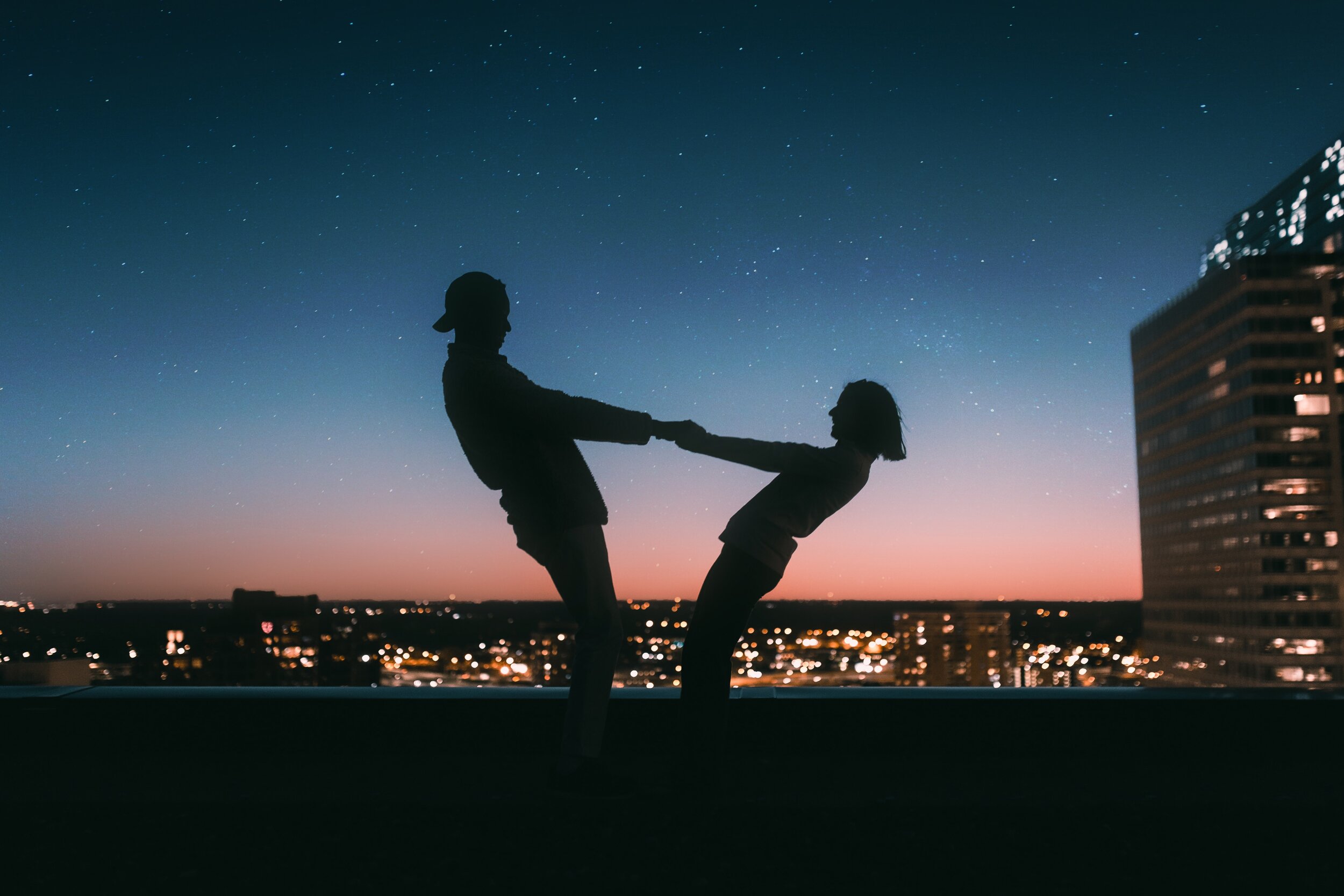 couple holding hands at sunset with the city lights behind them 