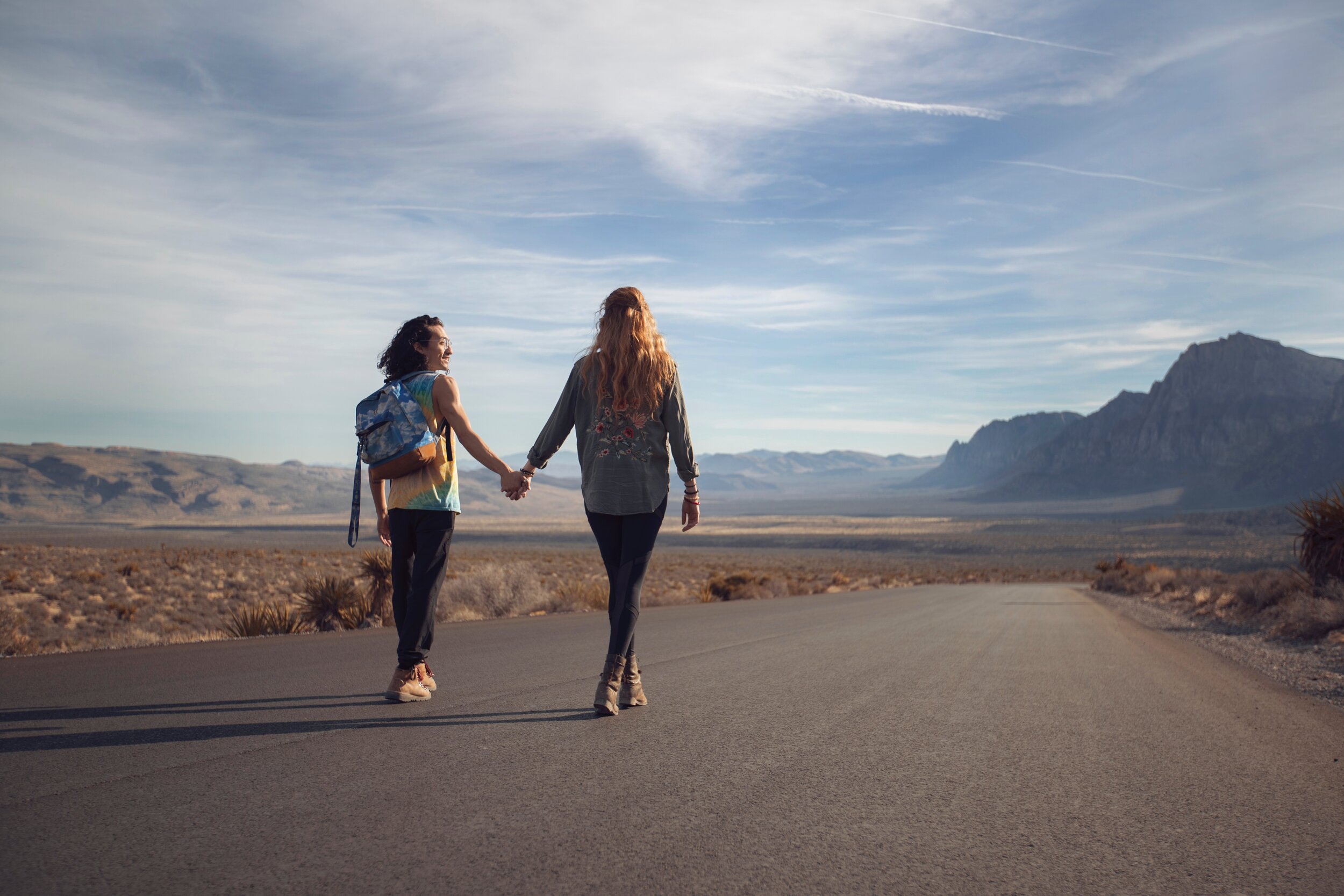 couple walking down a desert road holding hands. Image is captured from behind