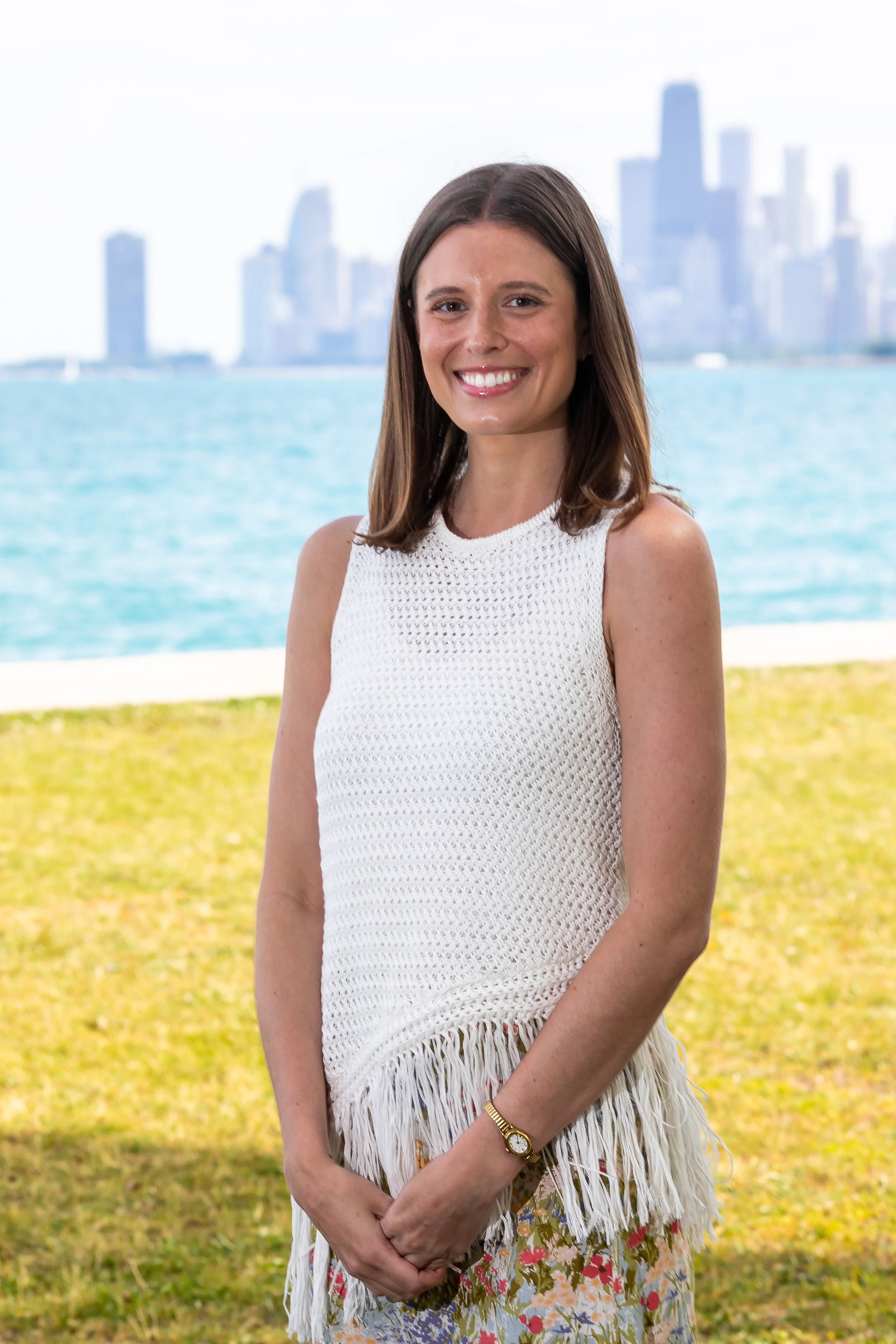 brunette white woman wedding coordinator wearing white stands on the grass in front of the chicago skyline on Lake Michigan