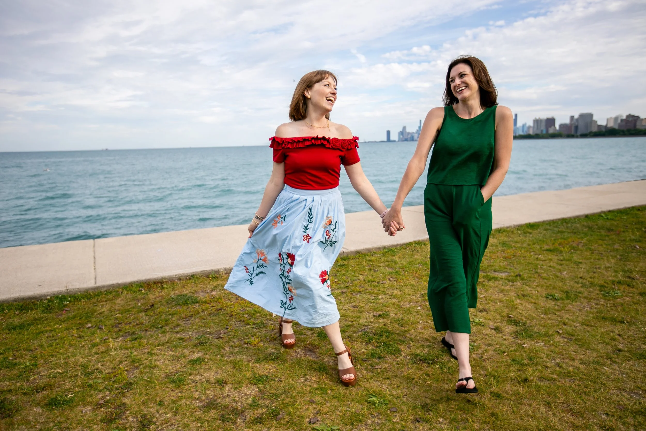 a redhead and a brunette woman hold hands in front of the chicago skyline on Lake Michigan