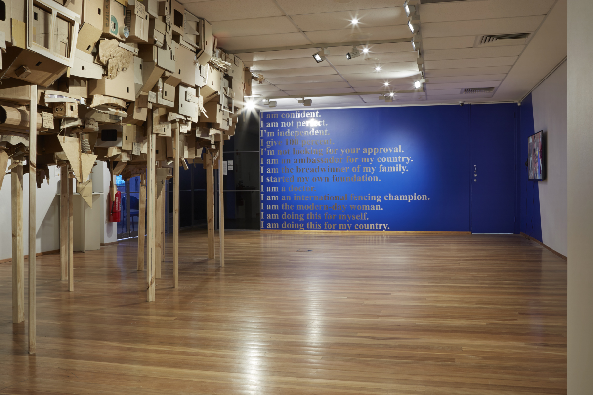 Confidently Beautiful, with a heart (background), 2017, video installation, with site-specific wall-painting and computer cut adhesive vinyl, video duration 8 minutes; Alfredo and Isabel Aqulizan, Head | Land: Project Another Country (foreground), 2017, site-specific construction installation with recycled transport cardboard boxes, installation view, Halò , Mosman Art Gallery, Sydney. Photo: Zan Wimberley. Copyright JD Reforma