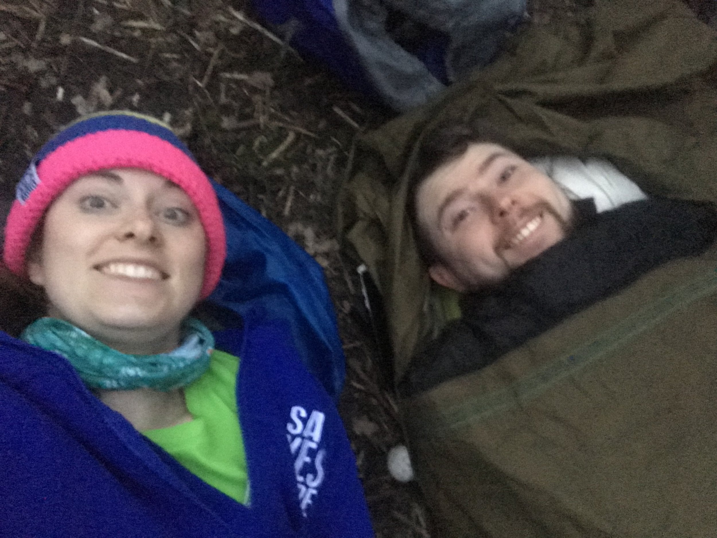 A photo of Jen and Ian in their sleeping bags bivvying in the woods
