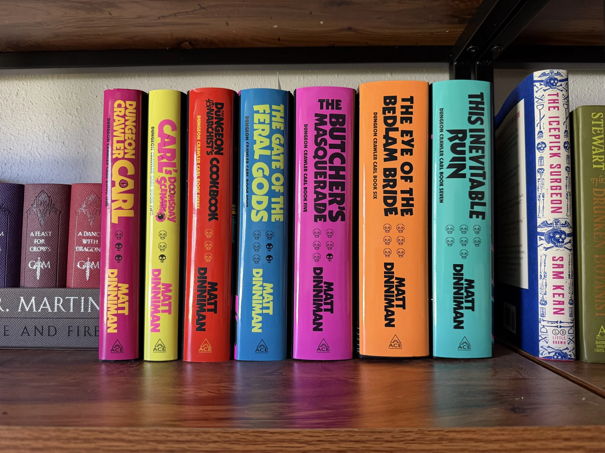 Books 1-7 of the Dungeon Crawler Carl series Ace editions nestled on a shelf next to A Song of Ice and Fire