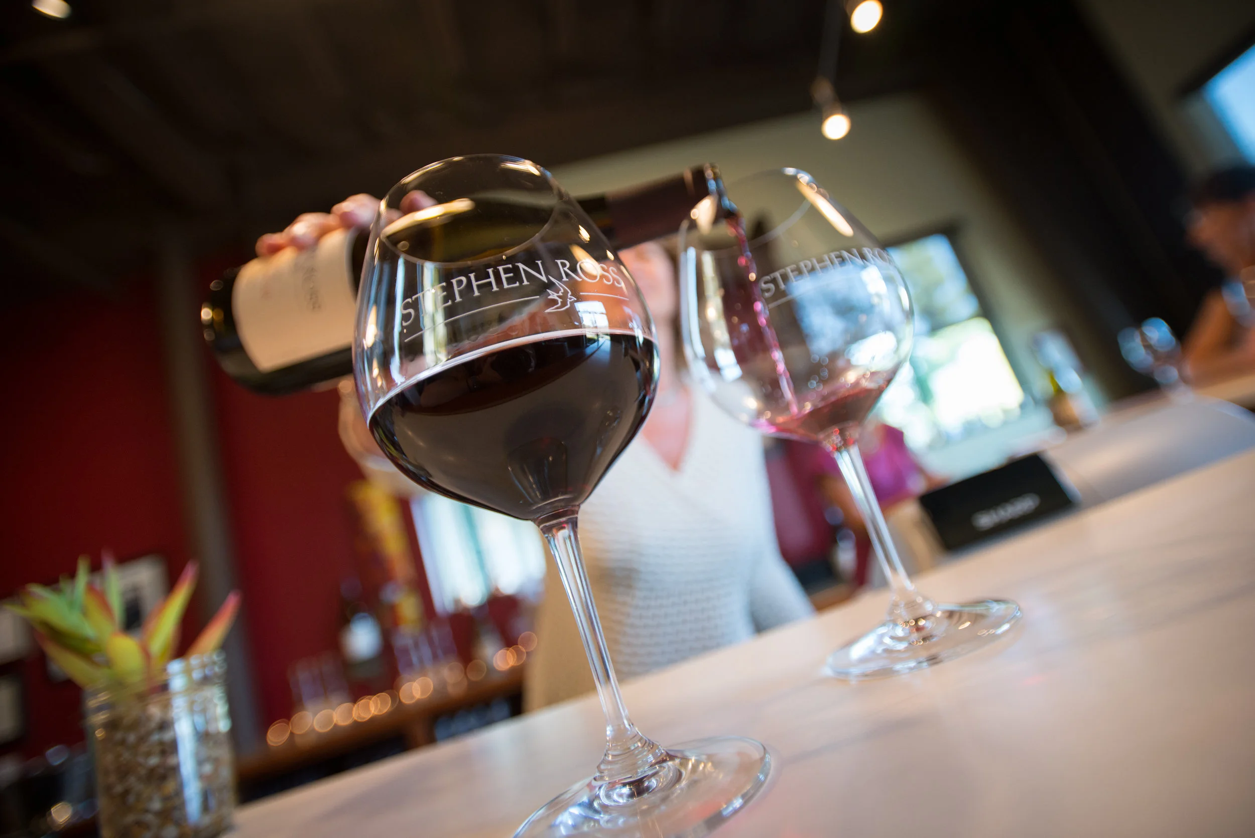 tasting room associate pouring two glasses of wine.