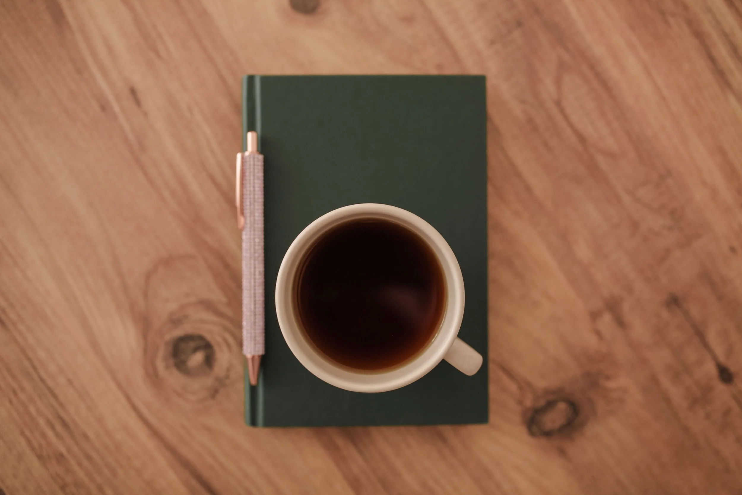 Journal, journaling pen, and cup of coffee sitting on a wooden table