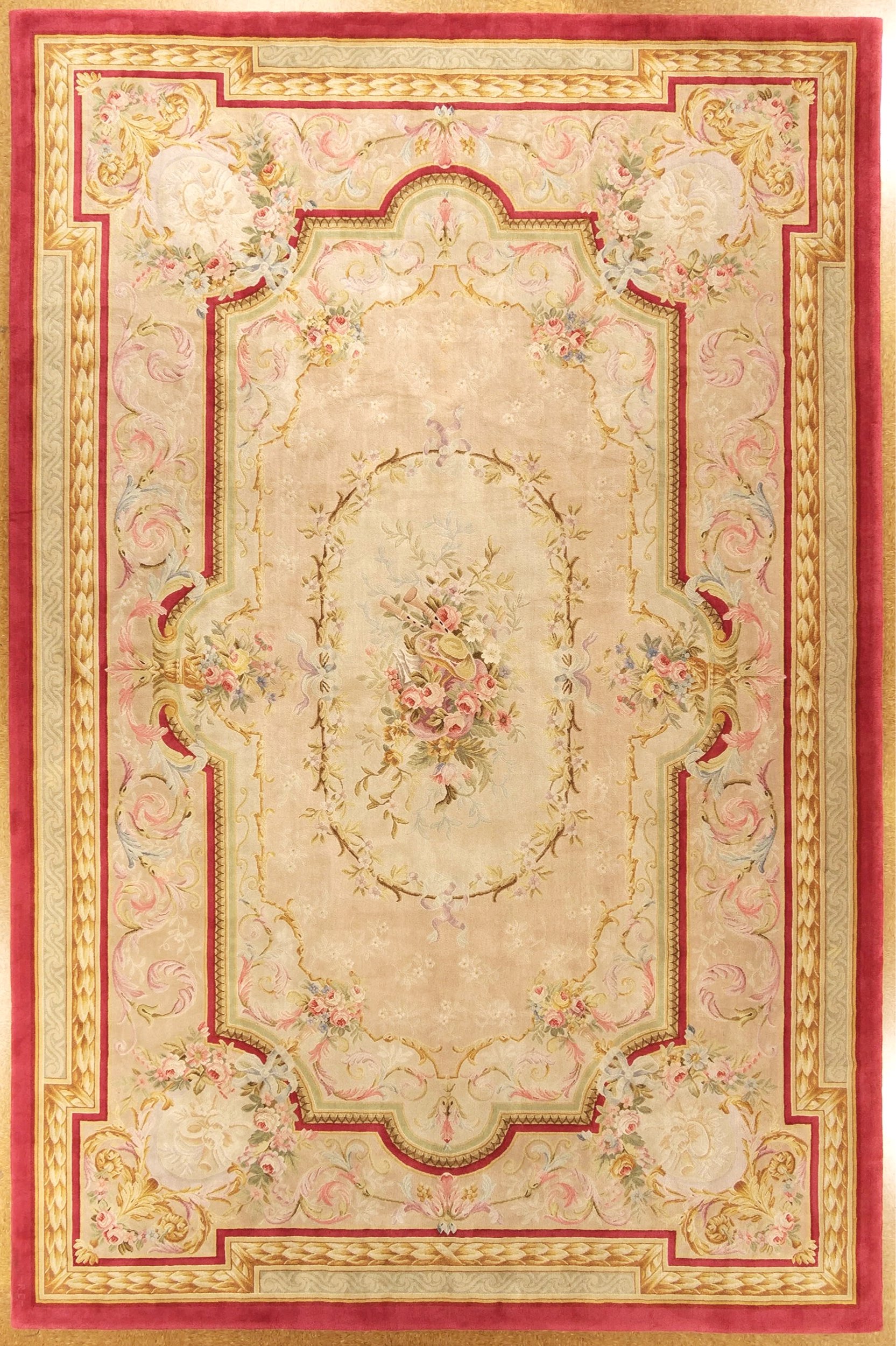 A traditional ornate Savonnerie rug with a champagne background, featuring floral patterns, a central bouquet, and decorative borders in shades of pink, gold, and red.