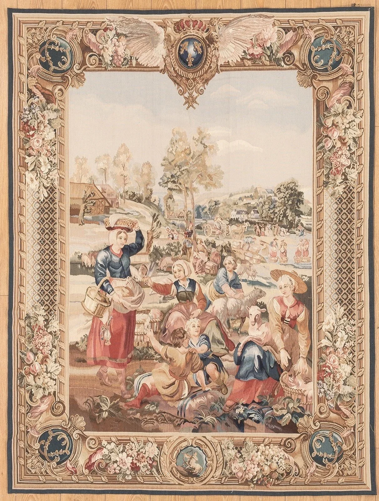 A  tapestry depicting a rural scene with children and women gathering around, tending to farm animals, and harvesting crops in a countryside landscape with trees, hills, and farms in the background. The border features intricate floral and scroll motifs with medallions
