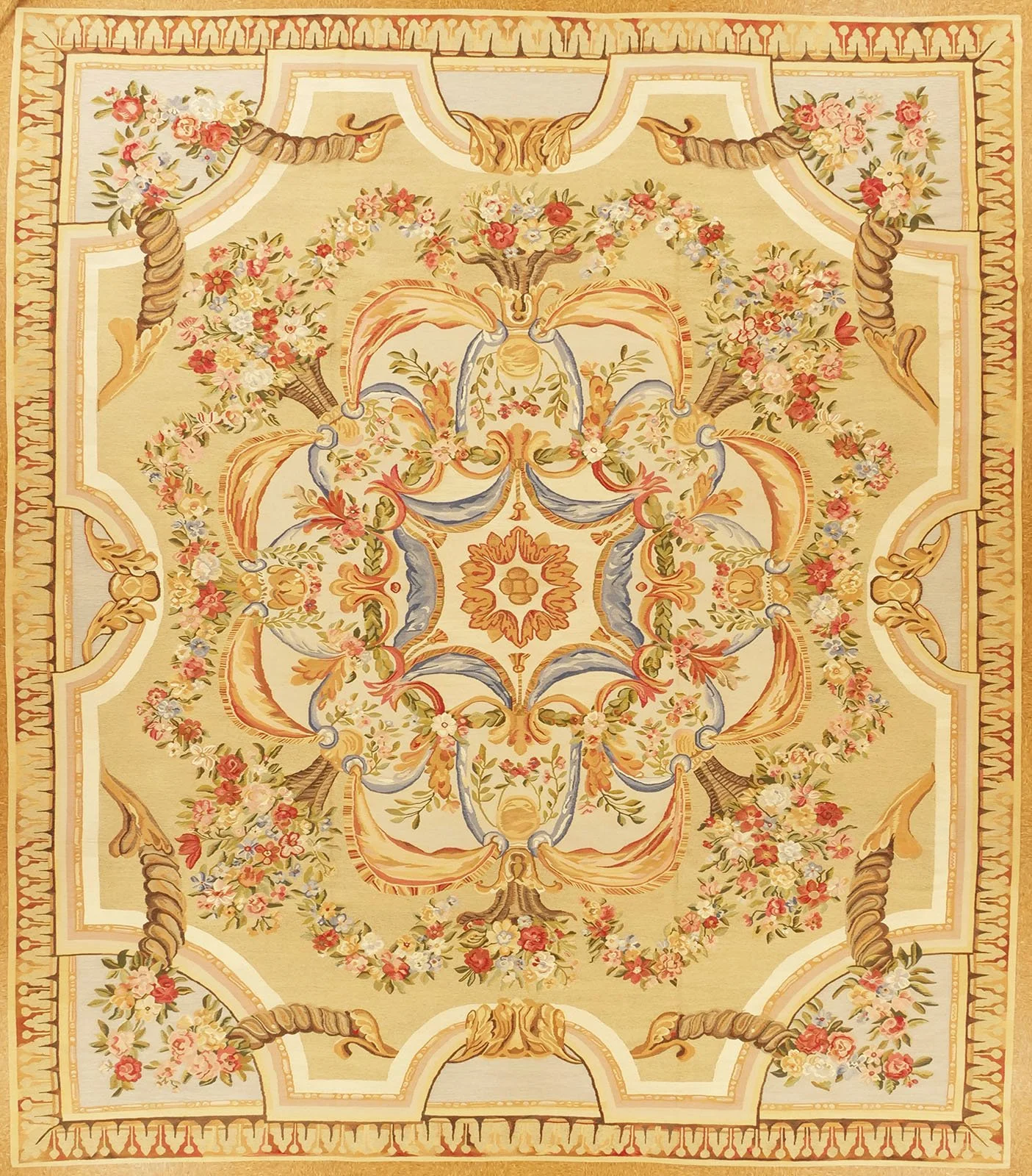 An ornate, floral-patterned rug with an intricate symmetrical design featuring flowers, scrolls, and decorative borders in shades of beige, pink, blue, and gold.