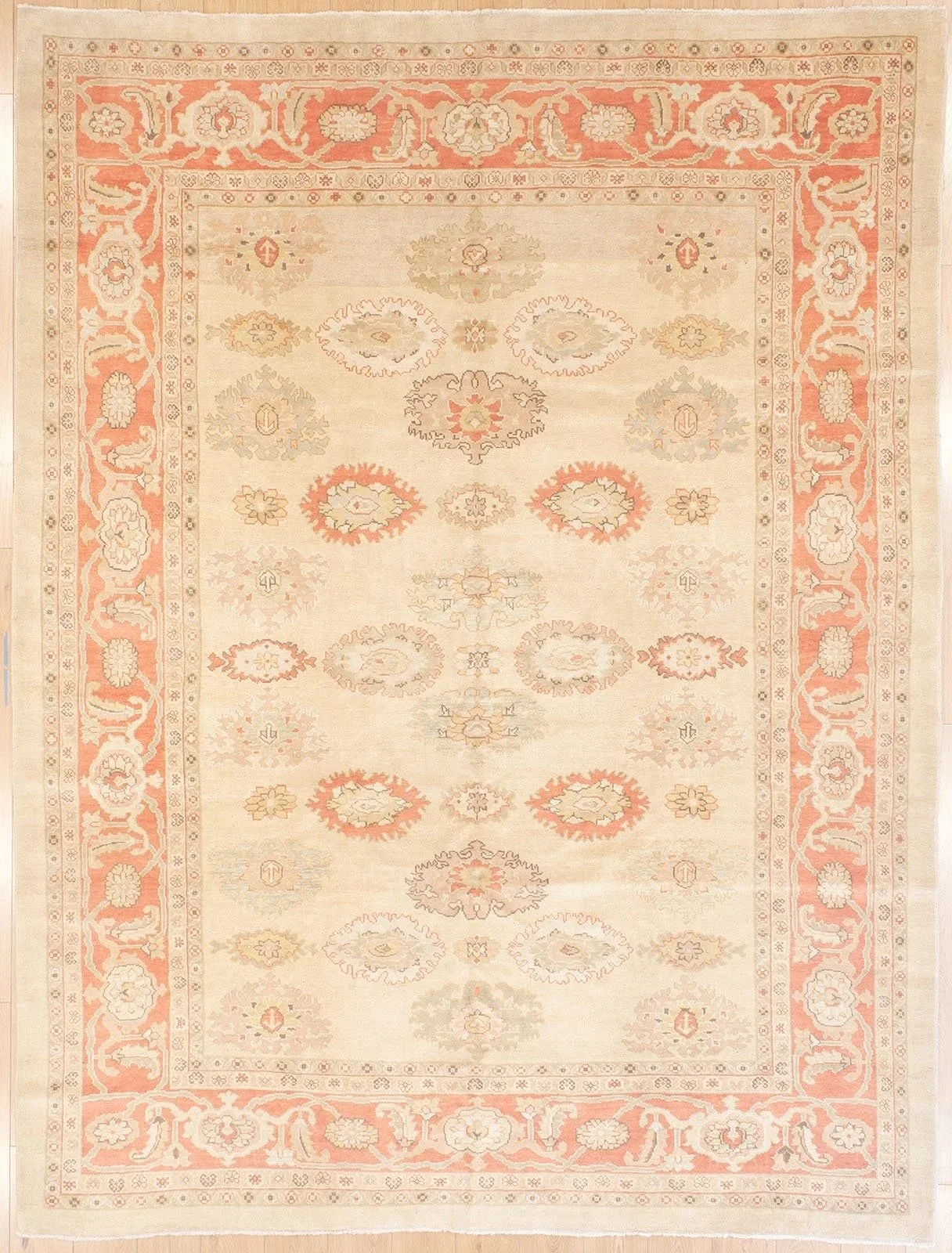 Persian, vintage area rug with a light beige background and intricate floral patterns in shades of pink, peach, light gray, and cream. The rug features a decorative border with floral motifs and a central pattern with symmetrical floral designs.