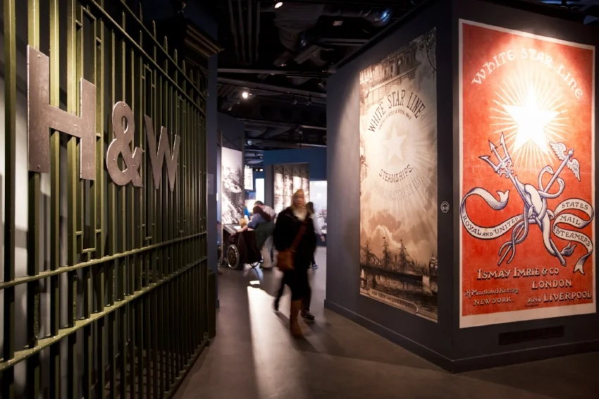 Harland & Wolff gates and White Star Line posters greet visitors as they begin the Titanic Experience with Boomtown Belfast . Image Credit: Titanic Belfast via Flickr CC