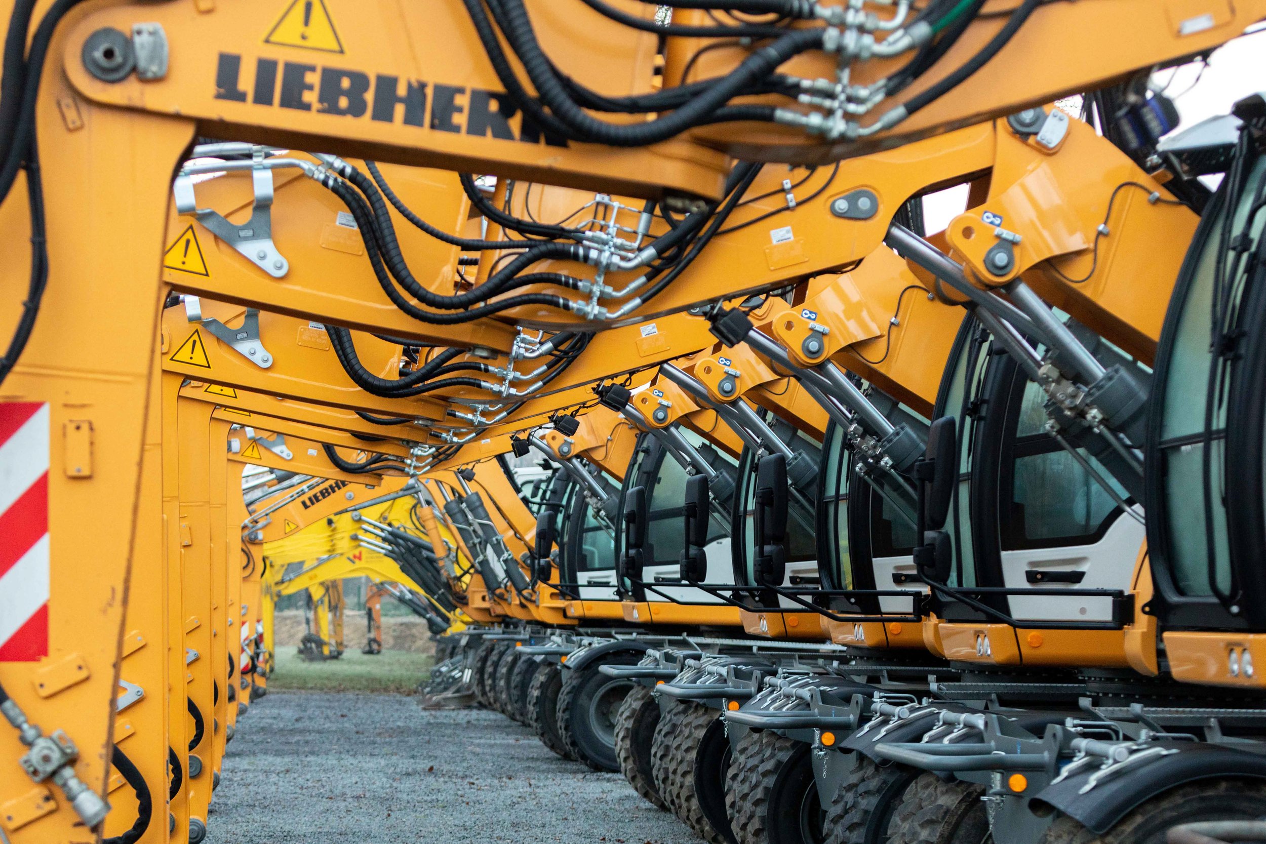 Une rangée de pelleteuses Caterpillar de couleur jaune stationnées en ligne, avec la marque Liebherr visible sur l'une d'elles, sur un terrain extérieur.