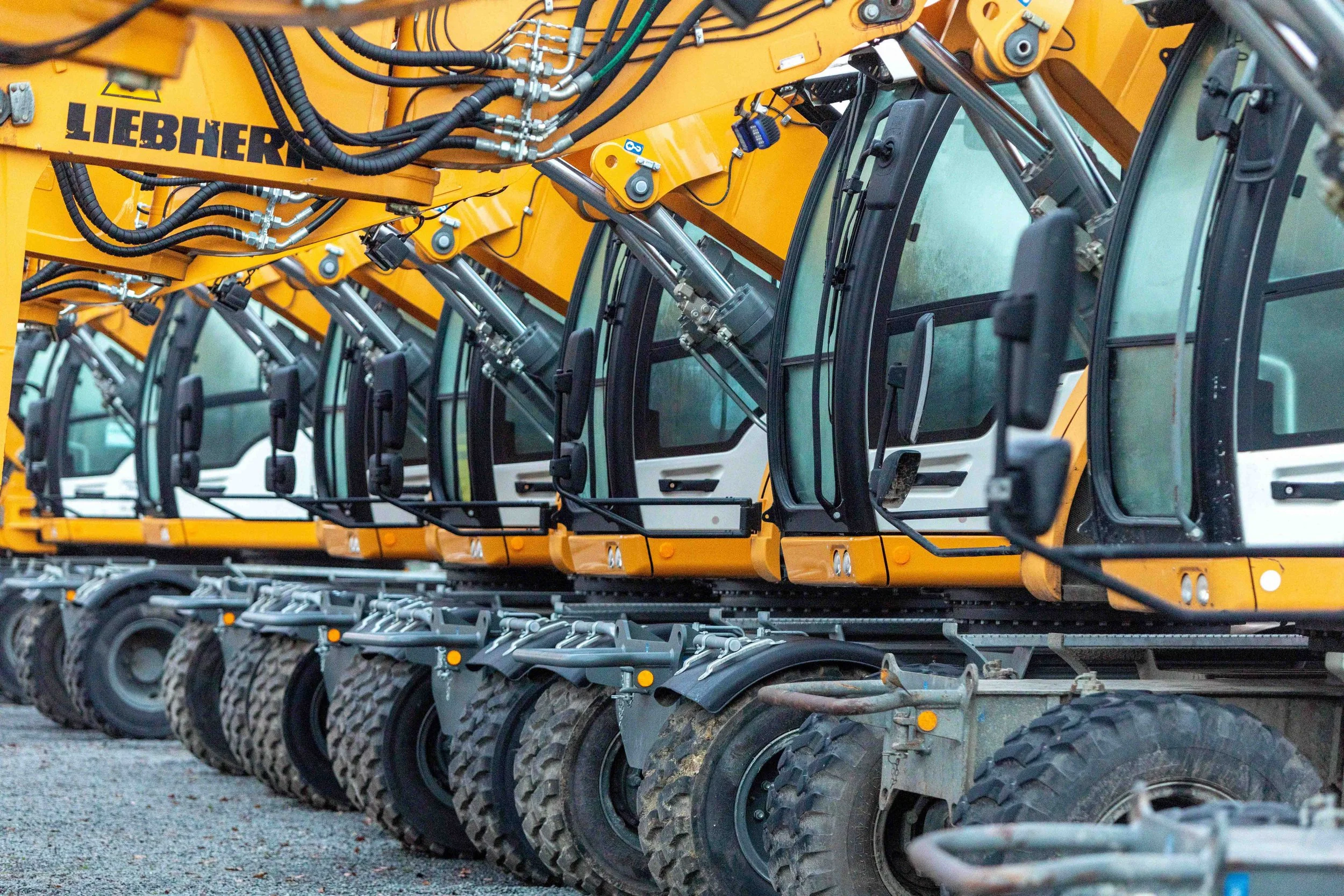 Une rangée de camions de construction jaunes alignés, montrant le bras hydraulique et les pneus.