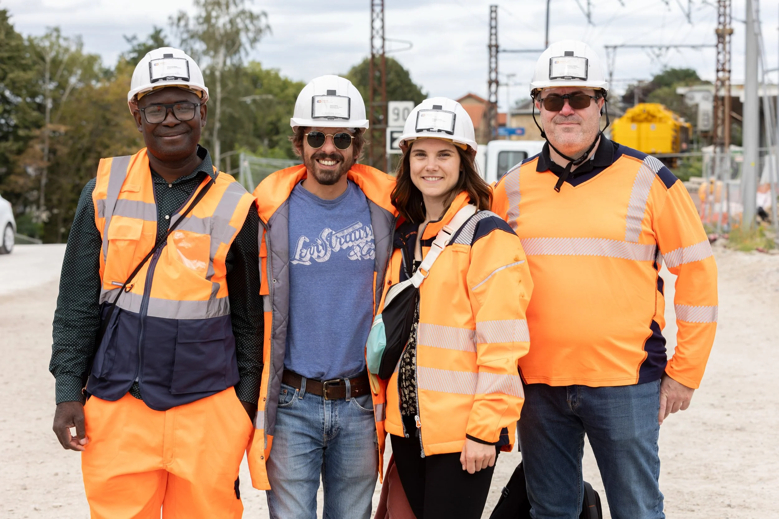 Groupe de quatre personnes portant des casques de sécurité et des gilets de haute visibilité dans un environnement industriel ou de construction.