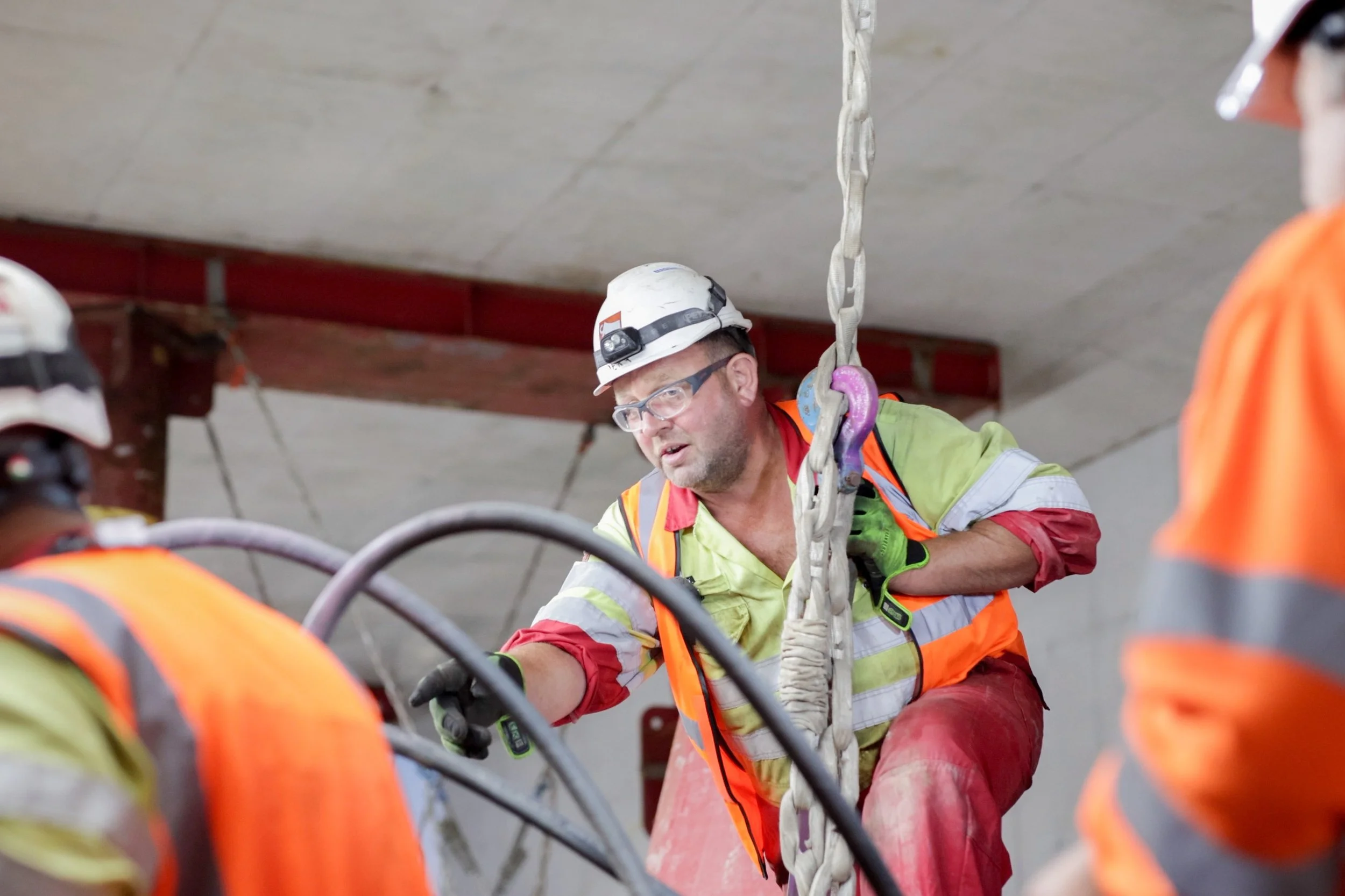 Travailleurs de construction portant des casques, vestes de sécurité et utilisant un équipement de levage à l'intérieur d'un bâtiment.