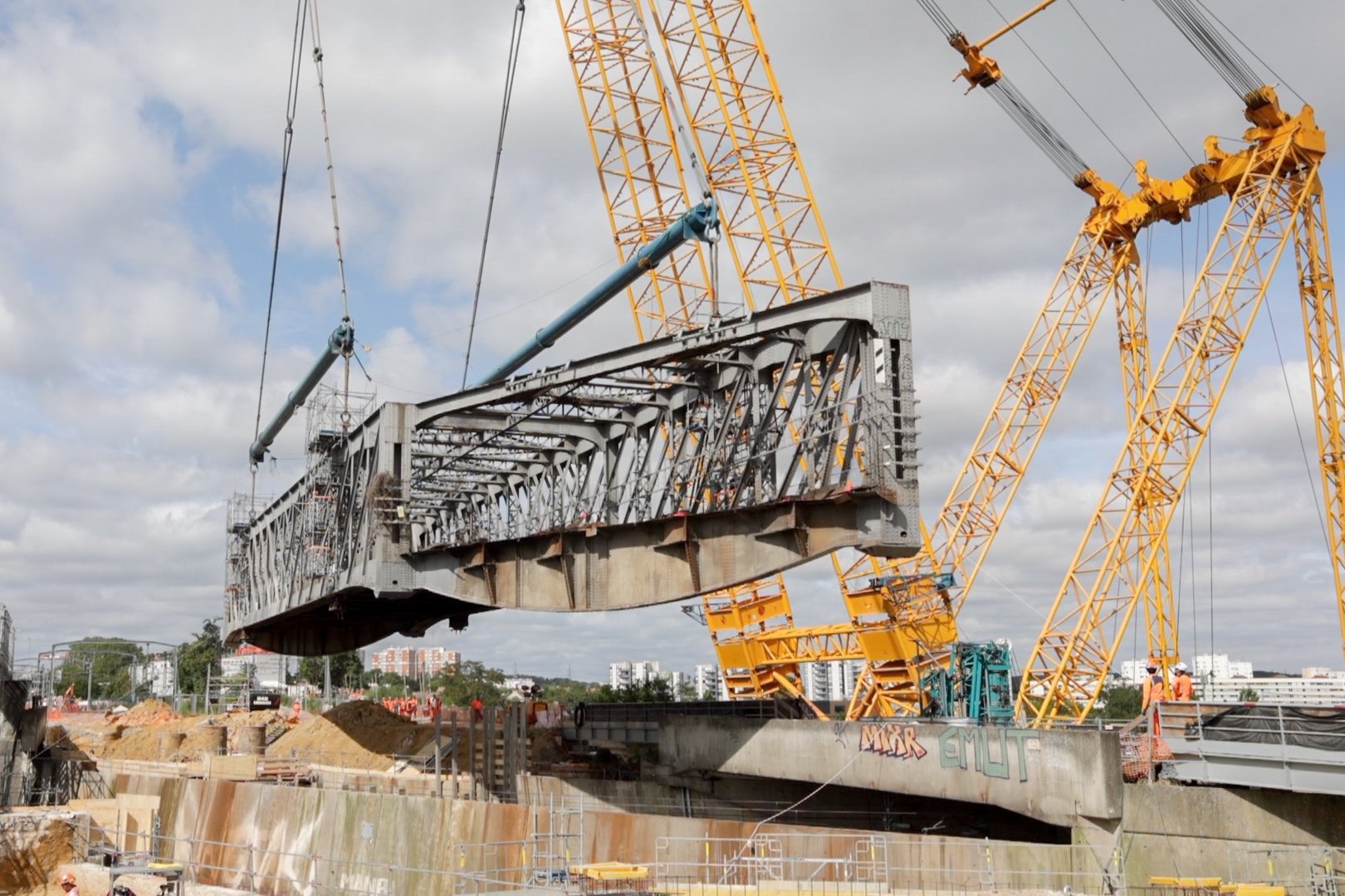 Une grue géante soulève une grande structure métallique sur un site de construction.