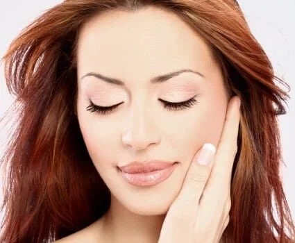 A red haired woman rubs the side of her faced with her eyes closed.