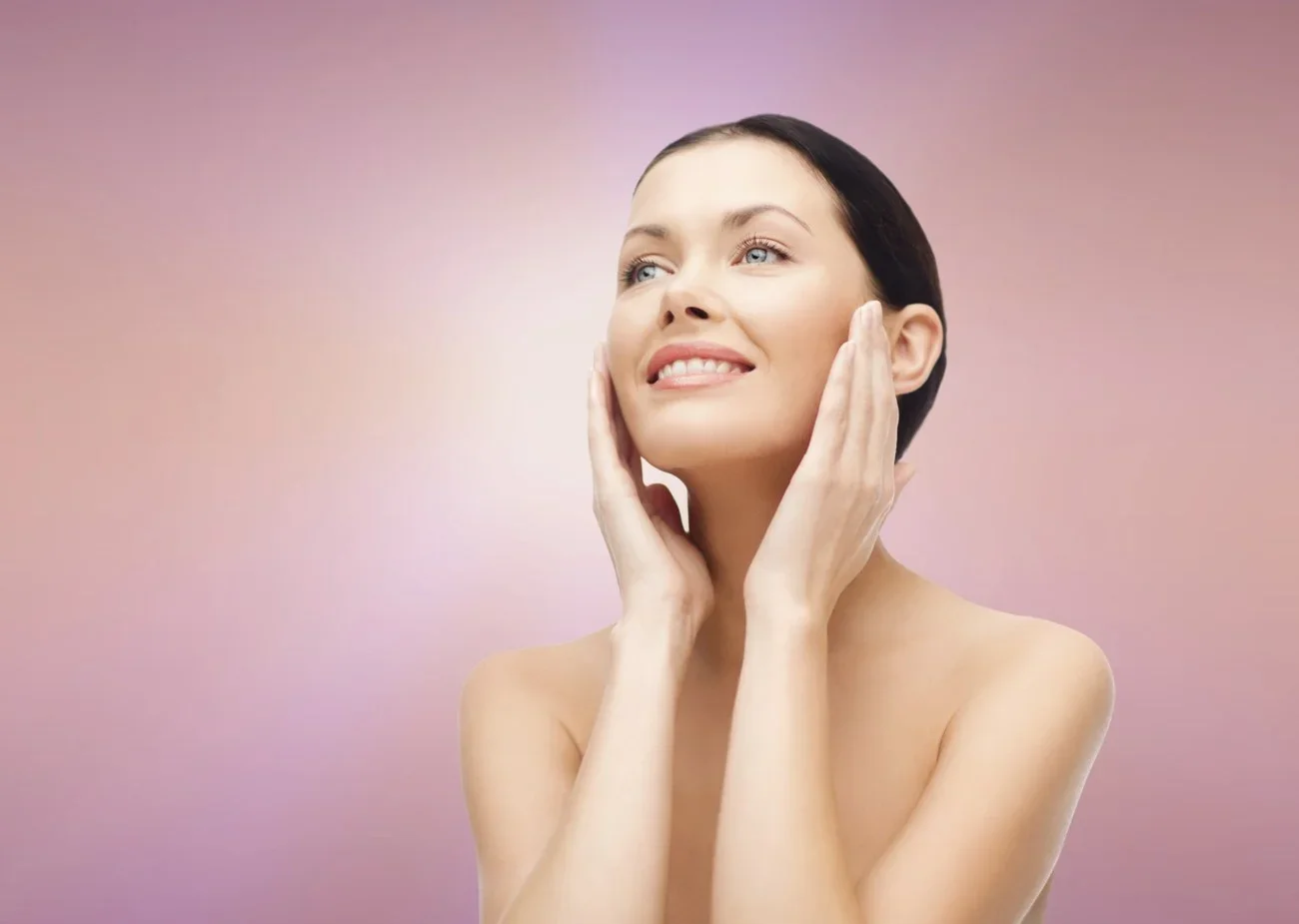 A pretty woman smiles and looks up, in front of a pink background.