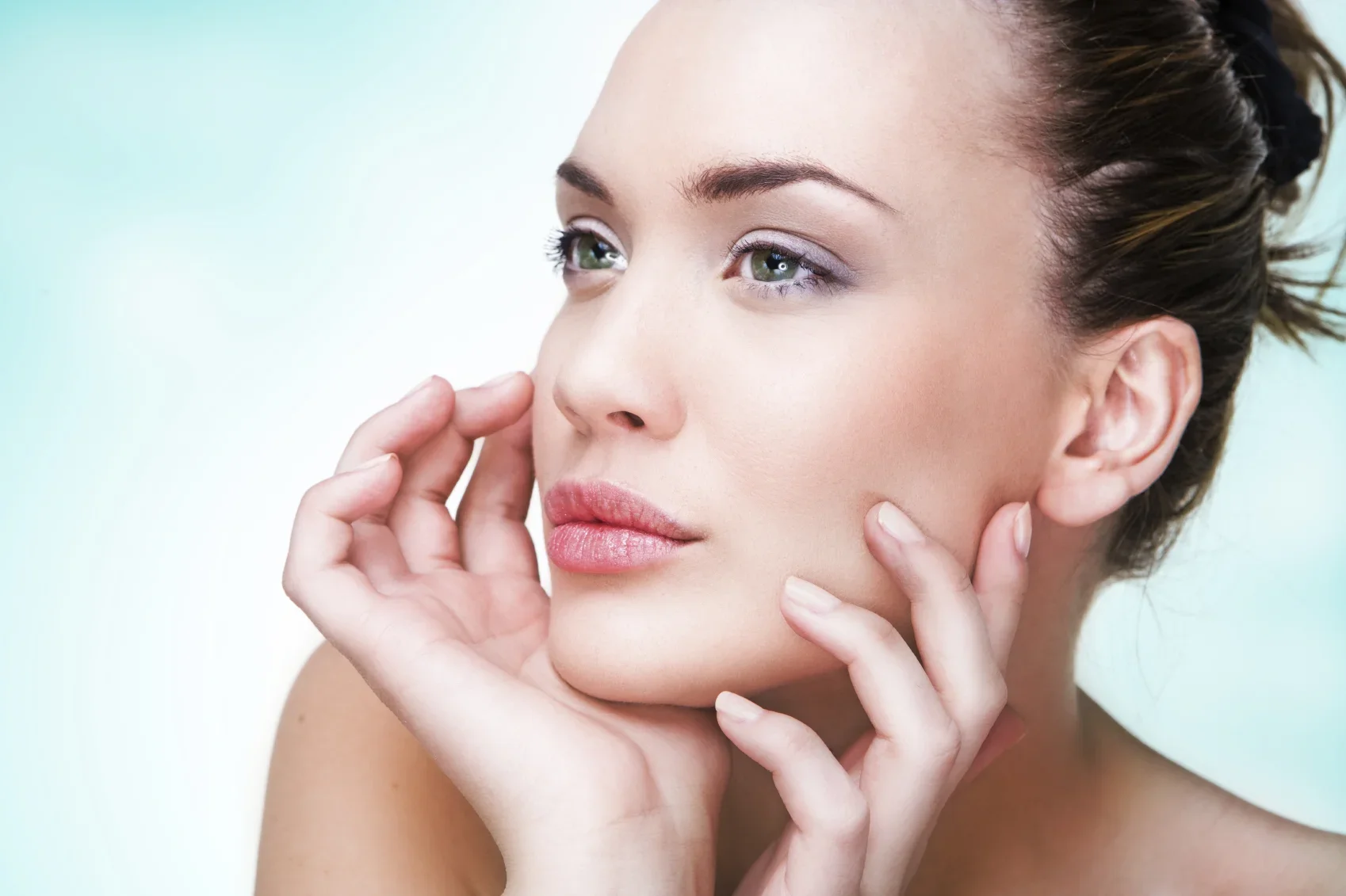 A woman looks to the left while touching her face with both hands.