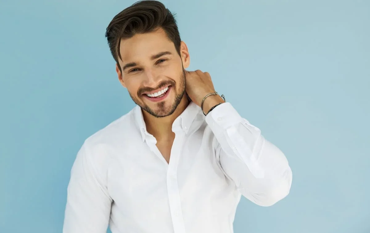 A dark-haired man smiles while rubbing his own neck.
