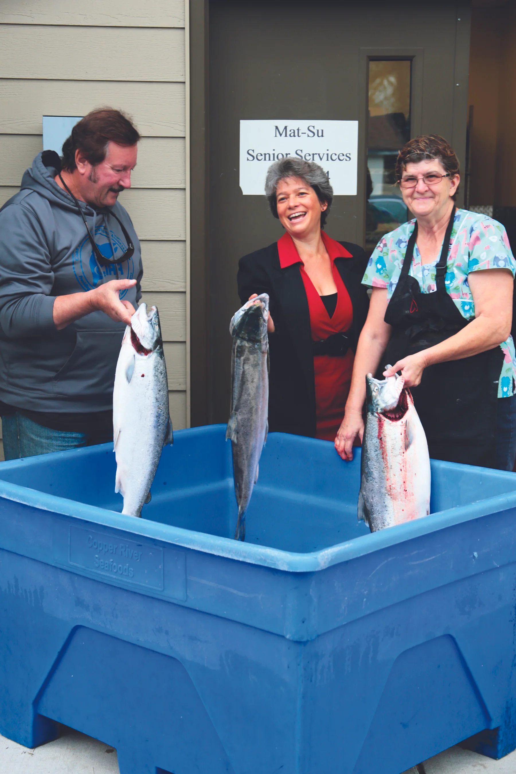   Bob Cellers of Northern District Setnetters, Mat-Su Senior Services Director, Rachel Greenberg, and Mat-Su Senior Services cook, Phyllis Moore. admire ‘Silvers for Seniors”.  
