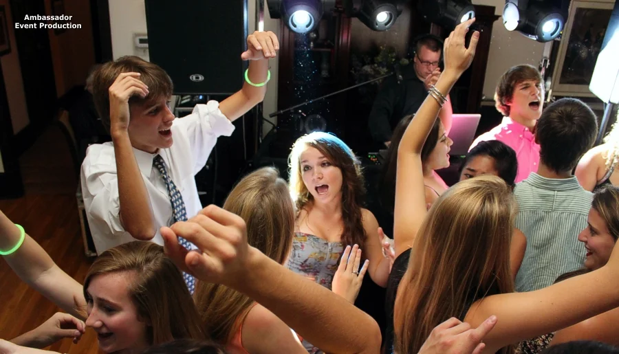 People dancing and having fun at a party or celebration, with a DJ playing music in the background.