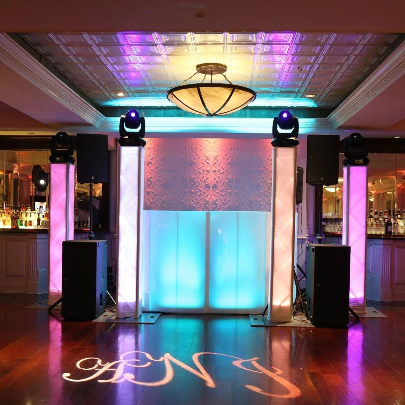 DJ booth with colorful LED lights, speakers, and lighting equipment in a decorated event space.