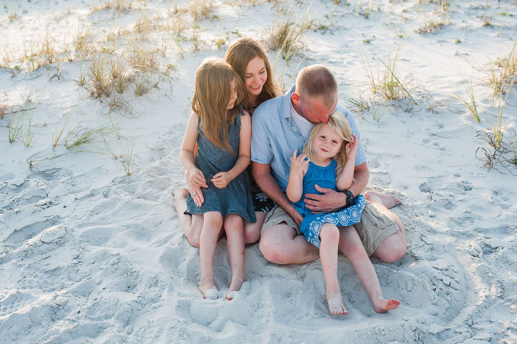family embracing on sand dunes by beach