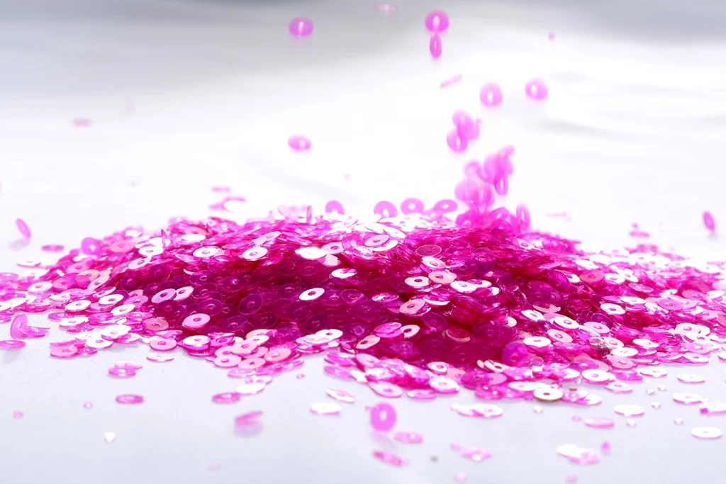 Pink sequins scattered on a white surface with some falling from above.