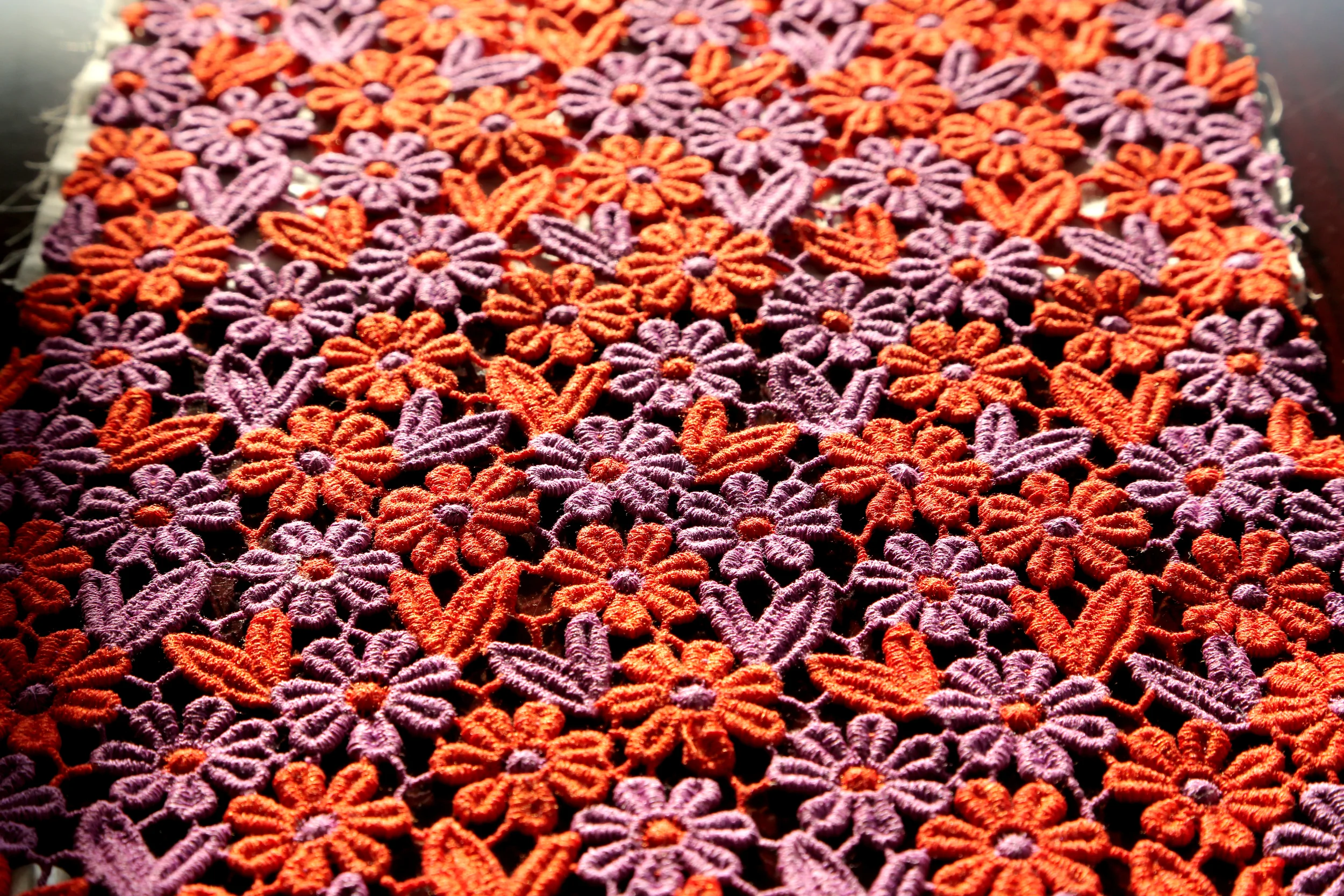 Close-up of a colorful crochet lace fabric with orange and purple floral patterns.
