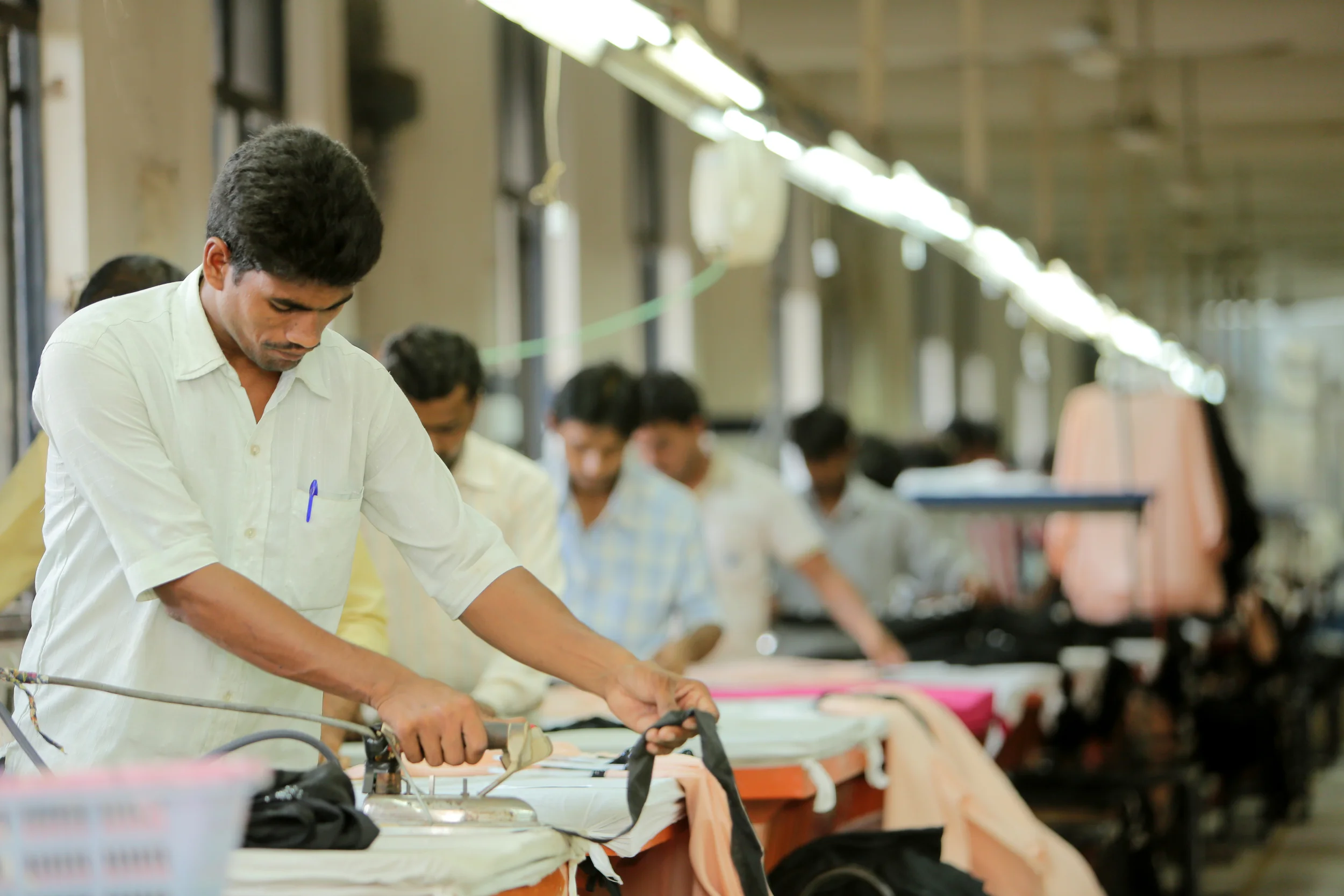 Workers in a clothing factory ironing fabric on tables in a workshop.