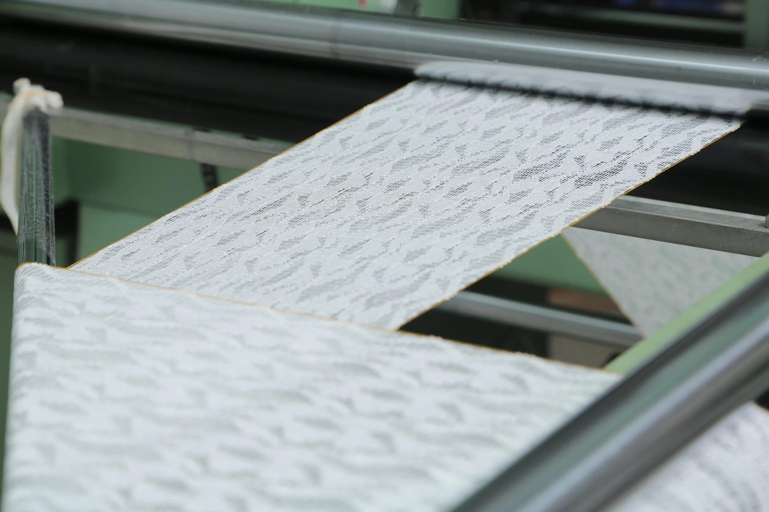 Close-up of white lace fabric being printed or woven on a machine.