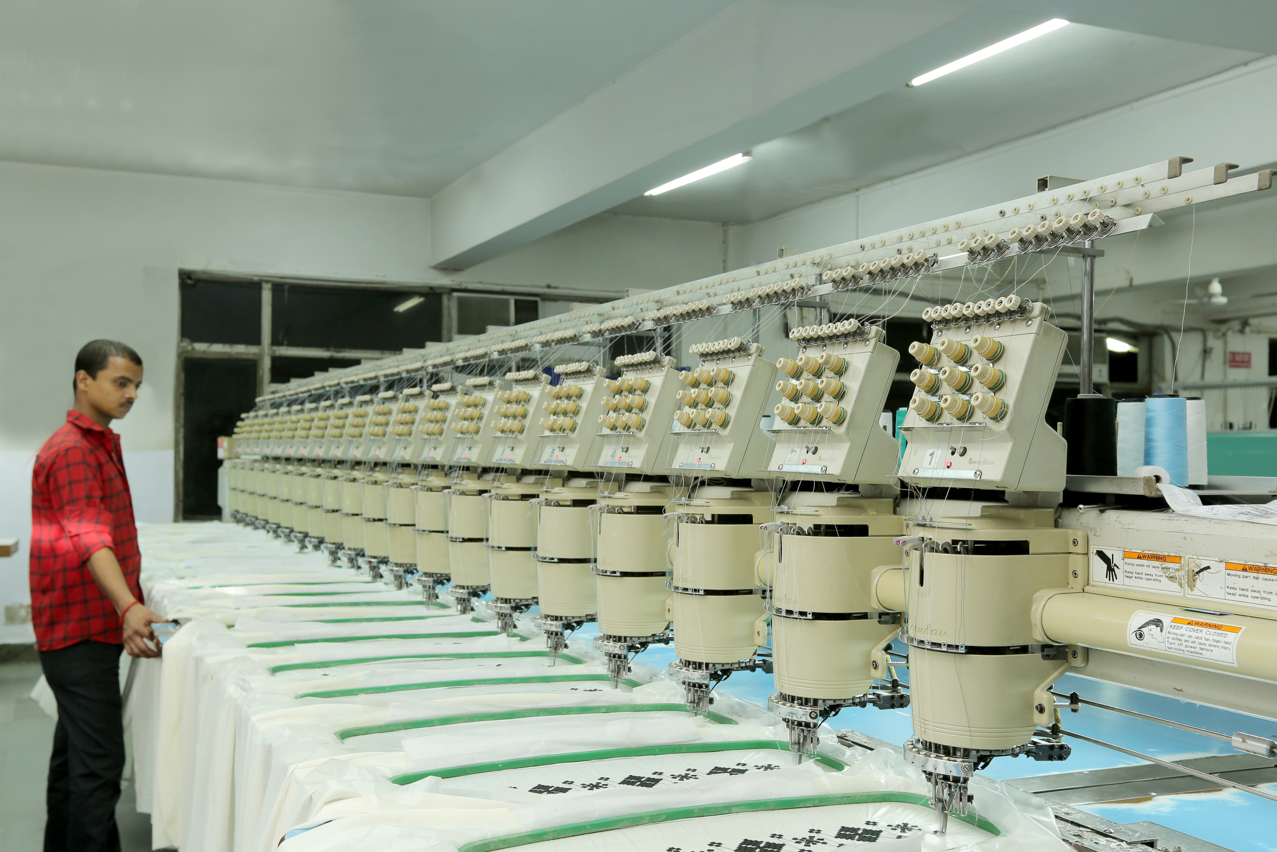 Worker in a red shirt operating embroidery machines in a factory.