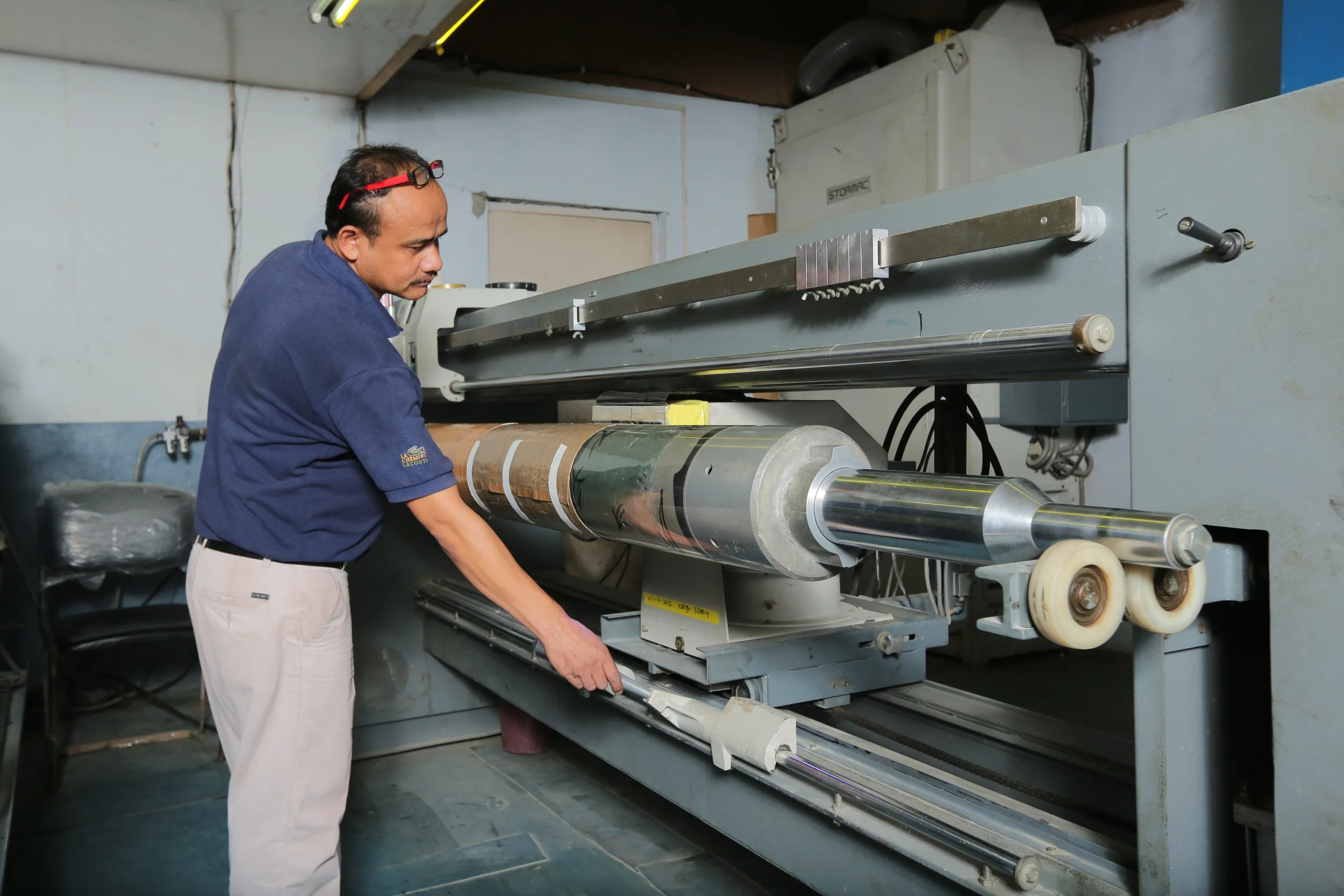 A man operating industrial machinery, specifically a large laminating or printing press, in a factory setting.