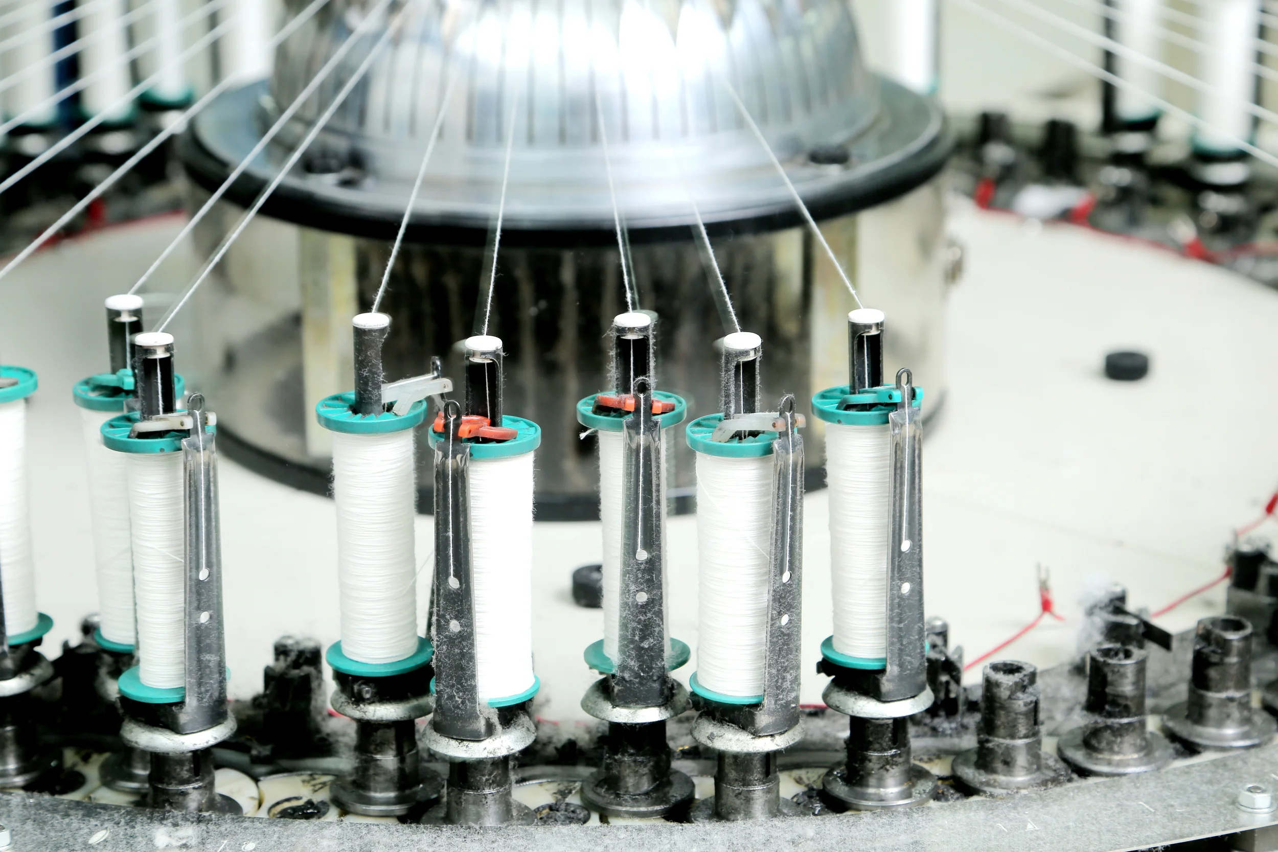 Close-up of a machine with multiple spools of white thread, part of a textile or sewing machine.