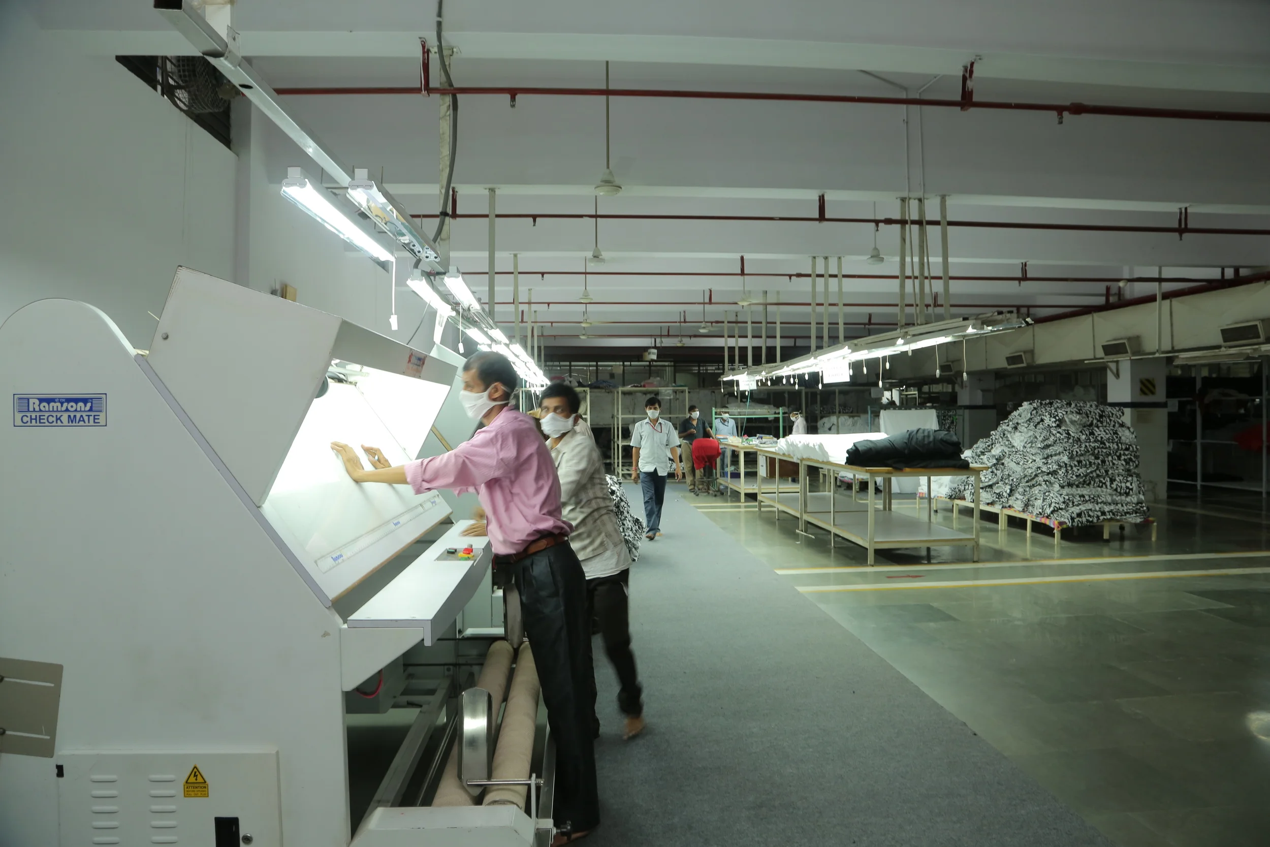Factory workers wearing masks operating a large industrial machine in a textile manufacturing facility.