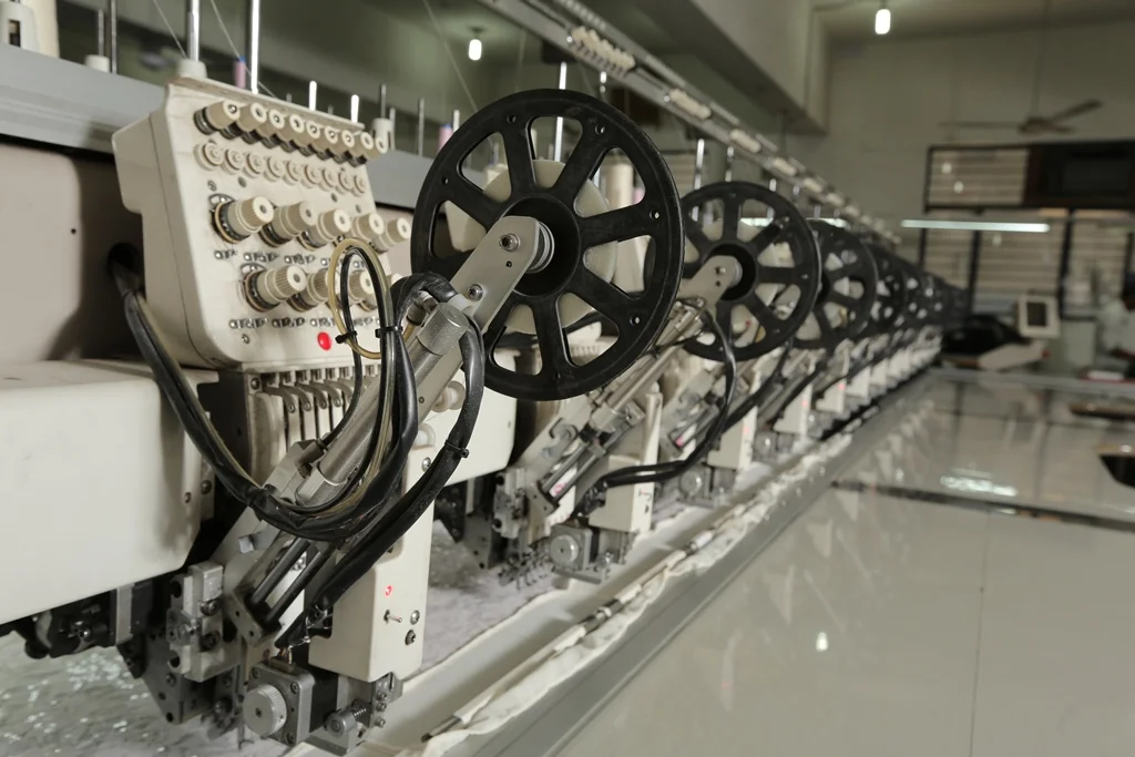 Industrial embroidery machine with multiple spools and wheels in a manufacturing setting.