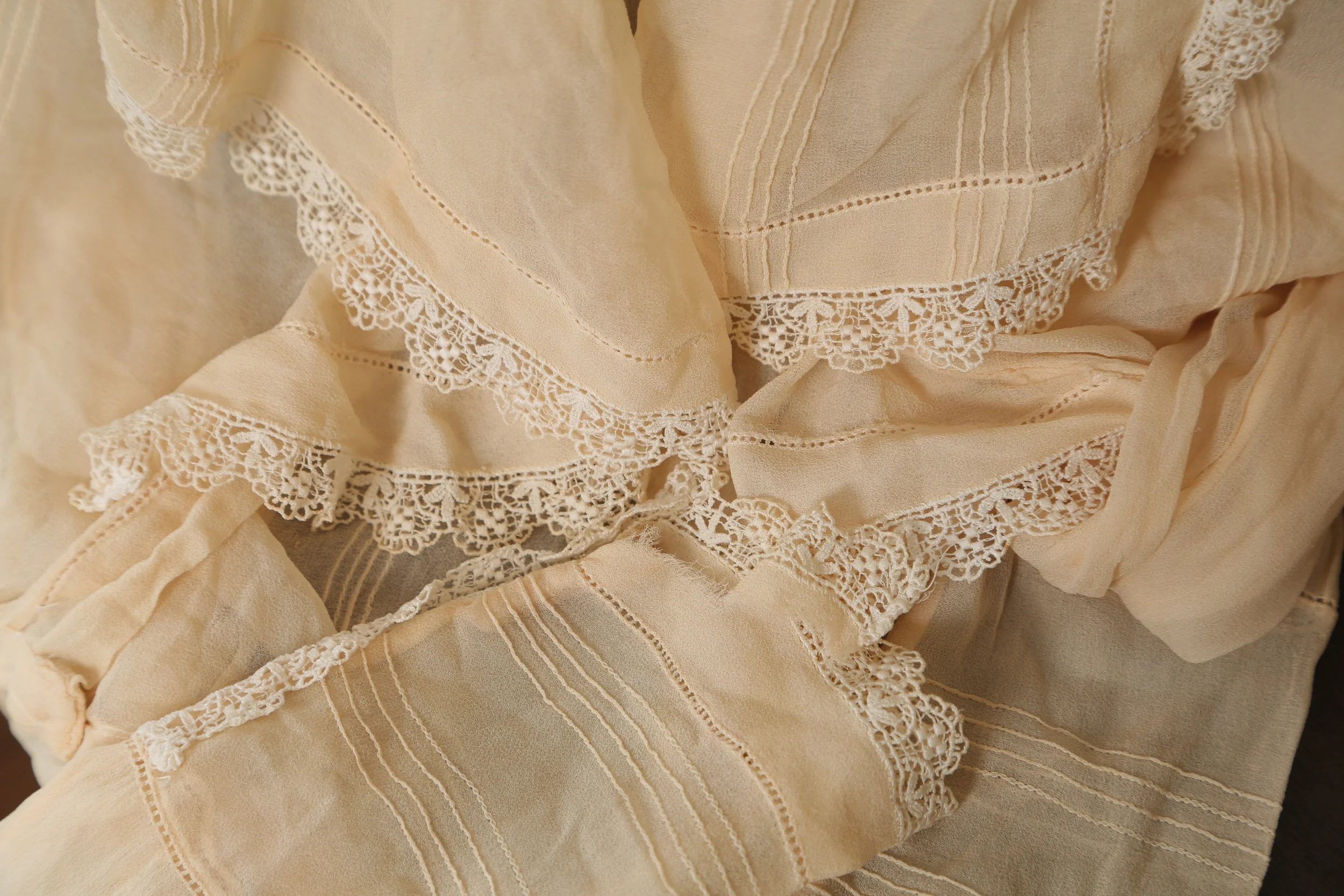 Close-up of vintage cream-colored lace-trimmed curtain fabric with delicate embroidery and scalloped edges.