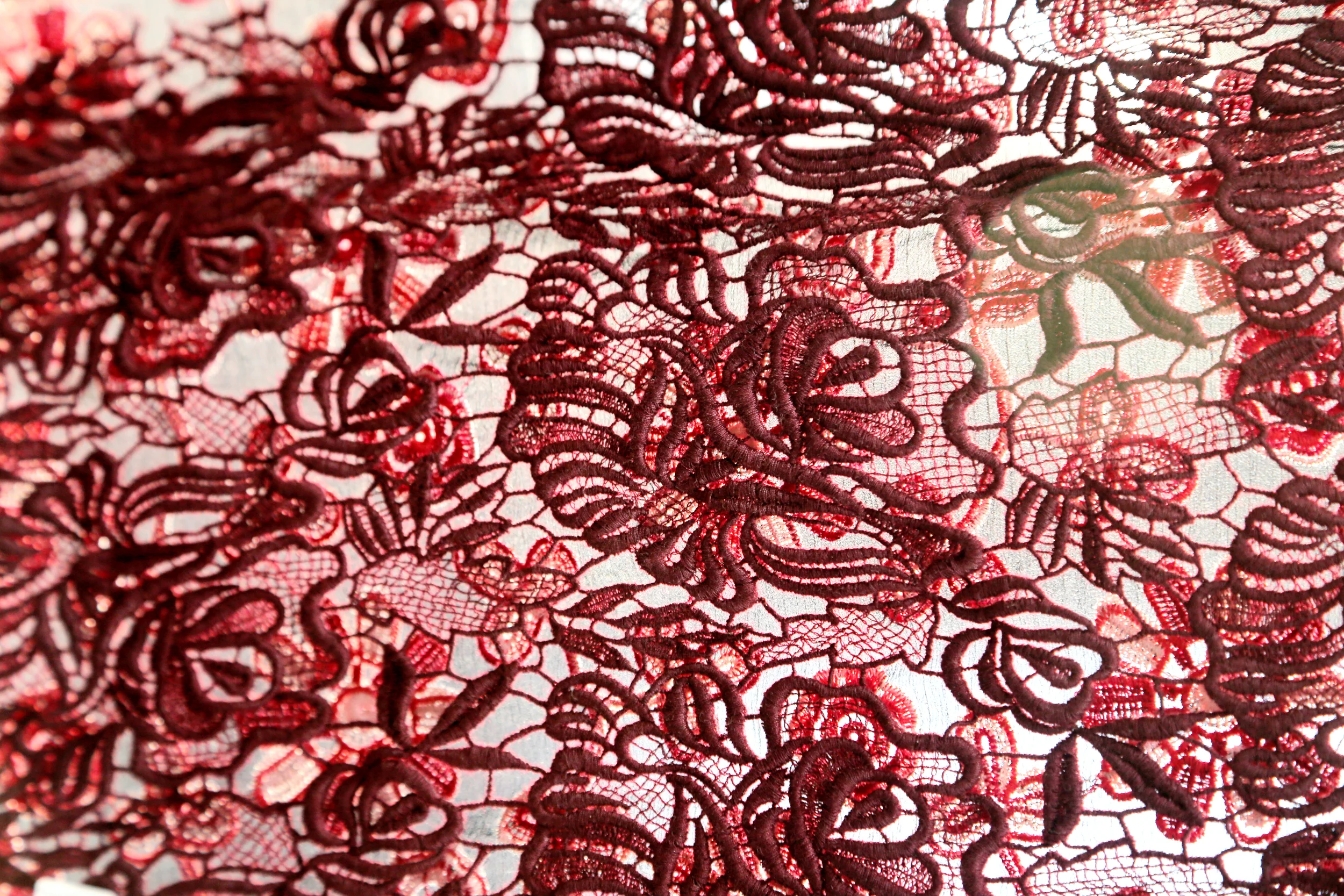 Close-up of red lace fabric with floral intricate pattern.