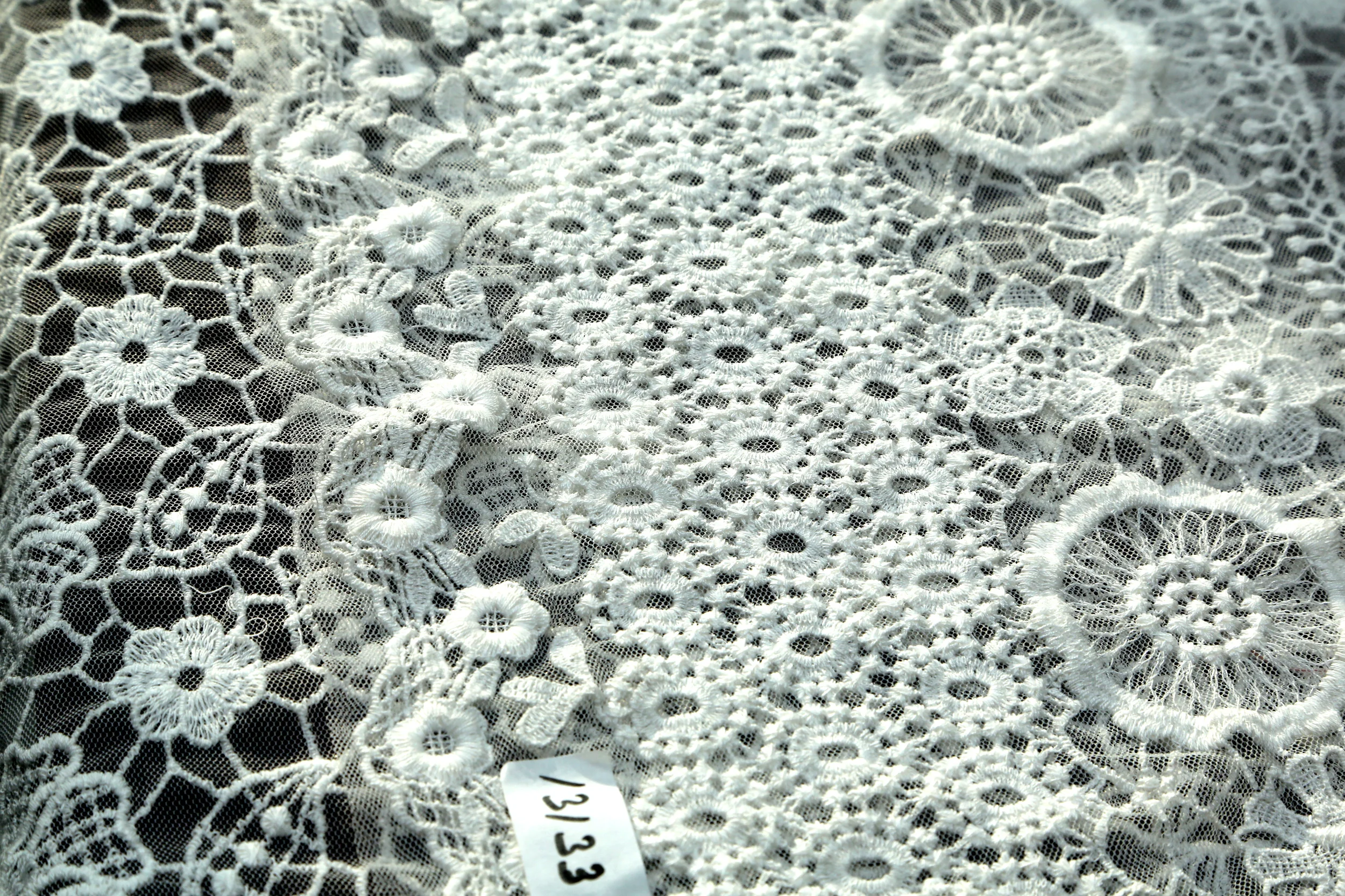 Close-up of white lace fabric with intricate floral patterns and a small white tag with black writing.