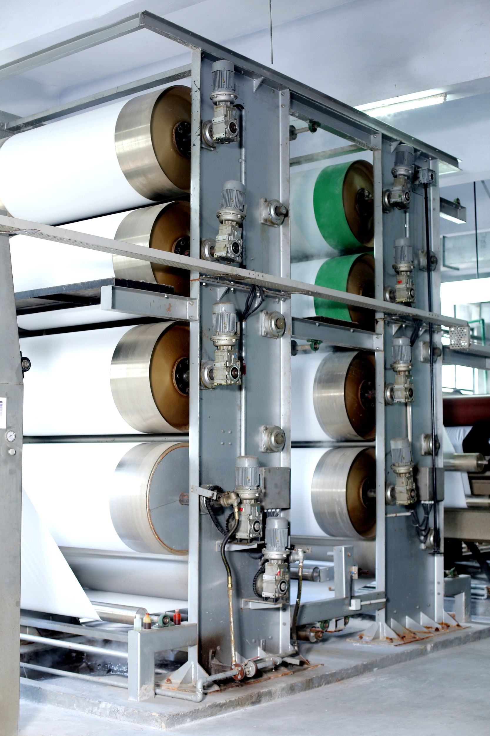 Industrial printing or paper manufacturing machine with large cylindrical rollers, some green and some white, and various mechanical components.