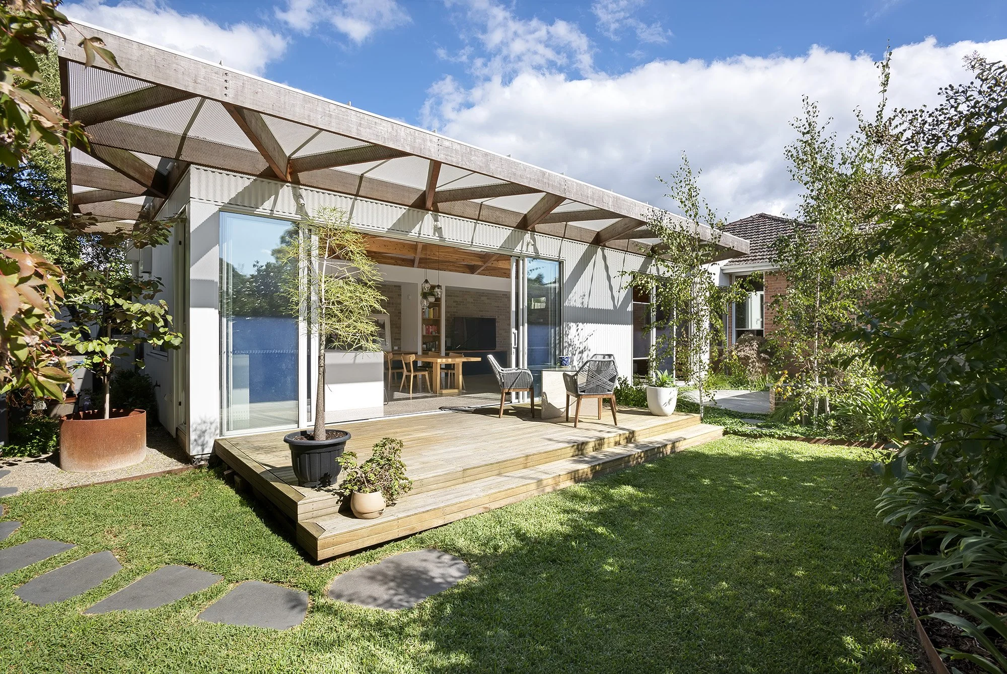 Rear extension with corrugated cladding and a perforated steel shading roof over a timber deck and established garden