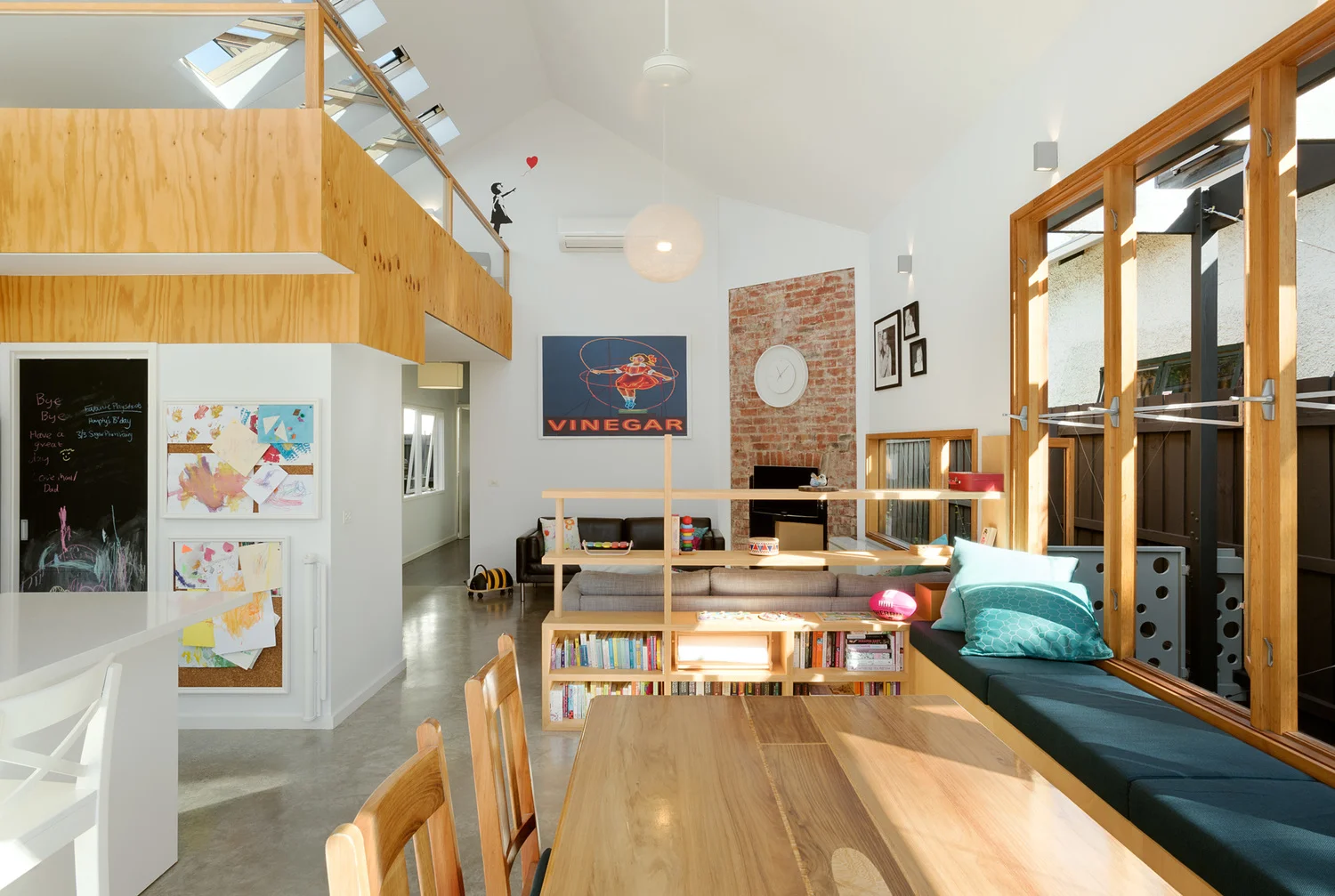 Living space beneath the plywood mezzanine and skylights, with a retained exposed brick chimney breast as a feature wall