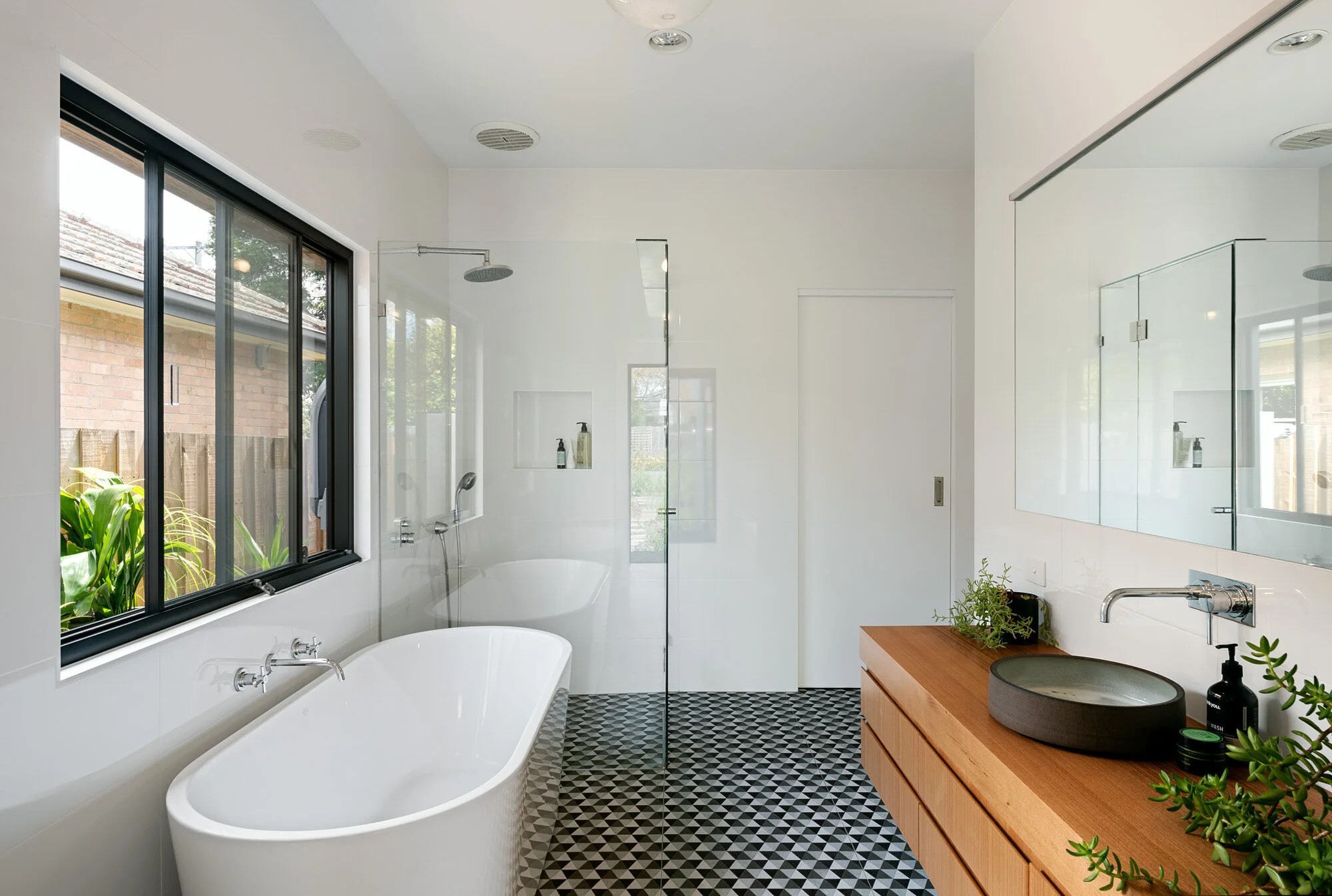 Bathroom with a geometric patterned floor, freestanding bath, walk-in shower and a timber vanity with a stone vessel basin