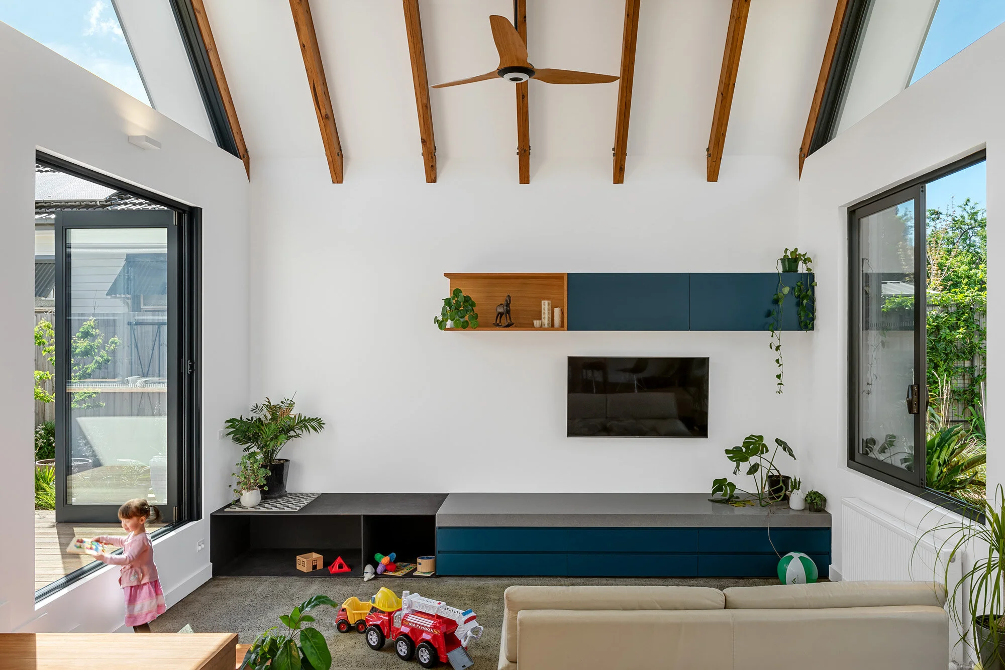 Living room with exposed raked timber rafters and a ceiling fan, opening to garden views on both sides